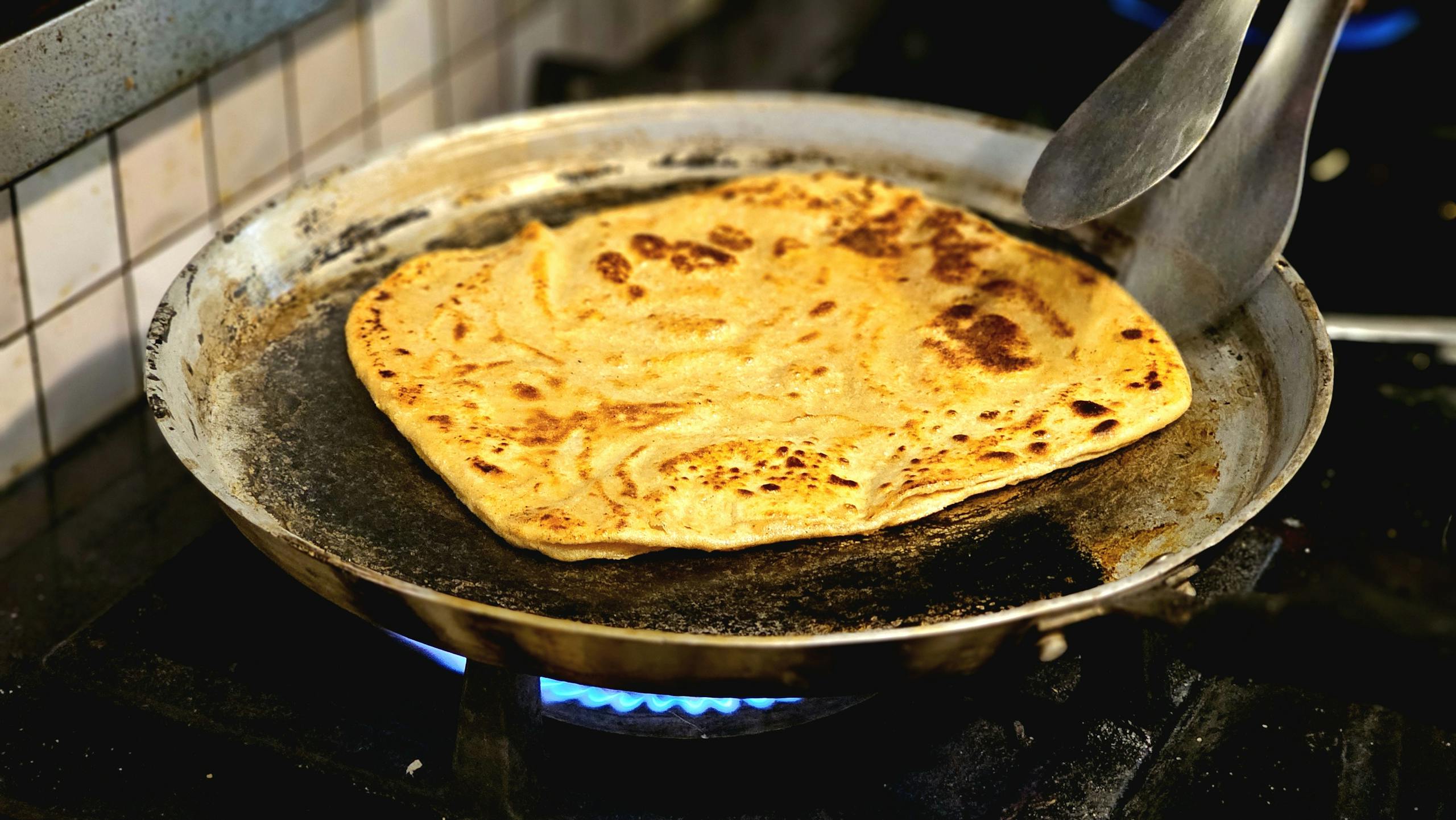 Golden brown paratha being cooked on a skillet, showcasing traditional flatbread preparation.