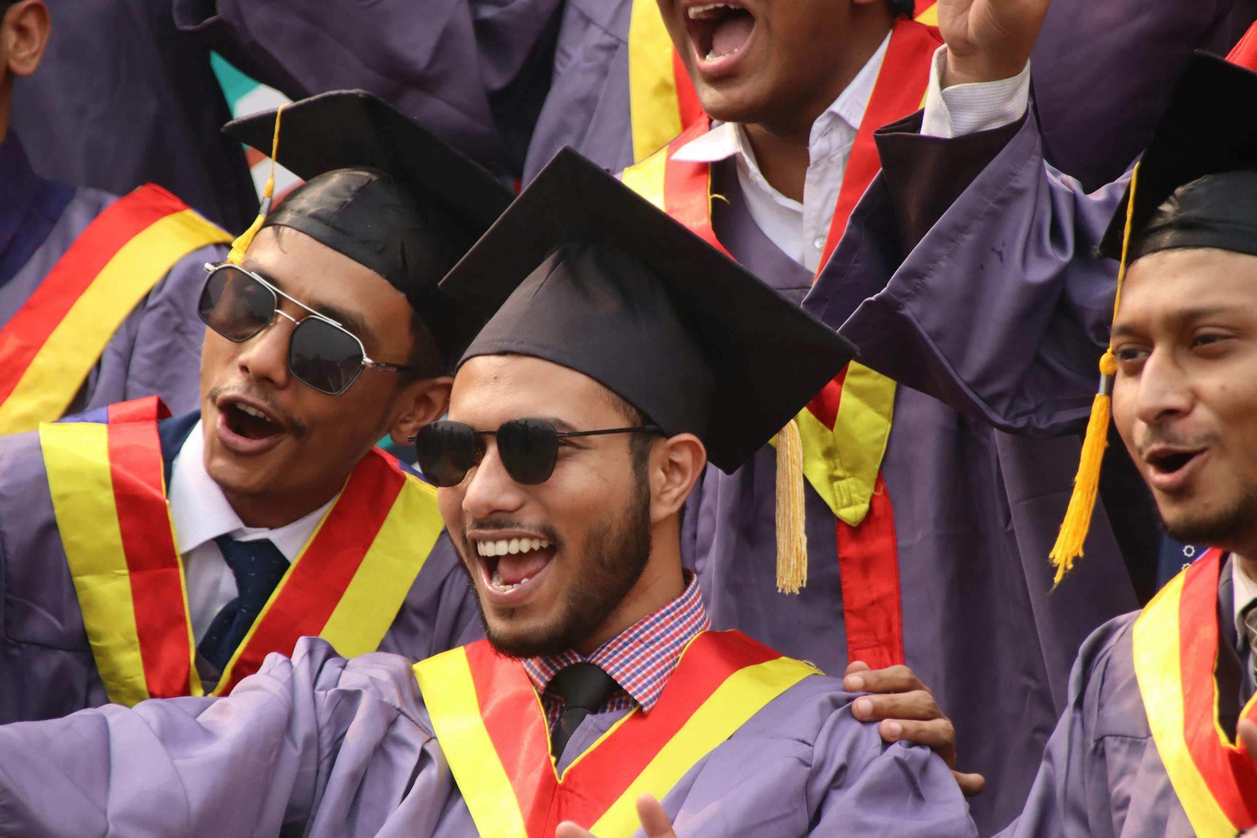 Group of diverse graduates celebrating with enthusiasm in convocation attire.