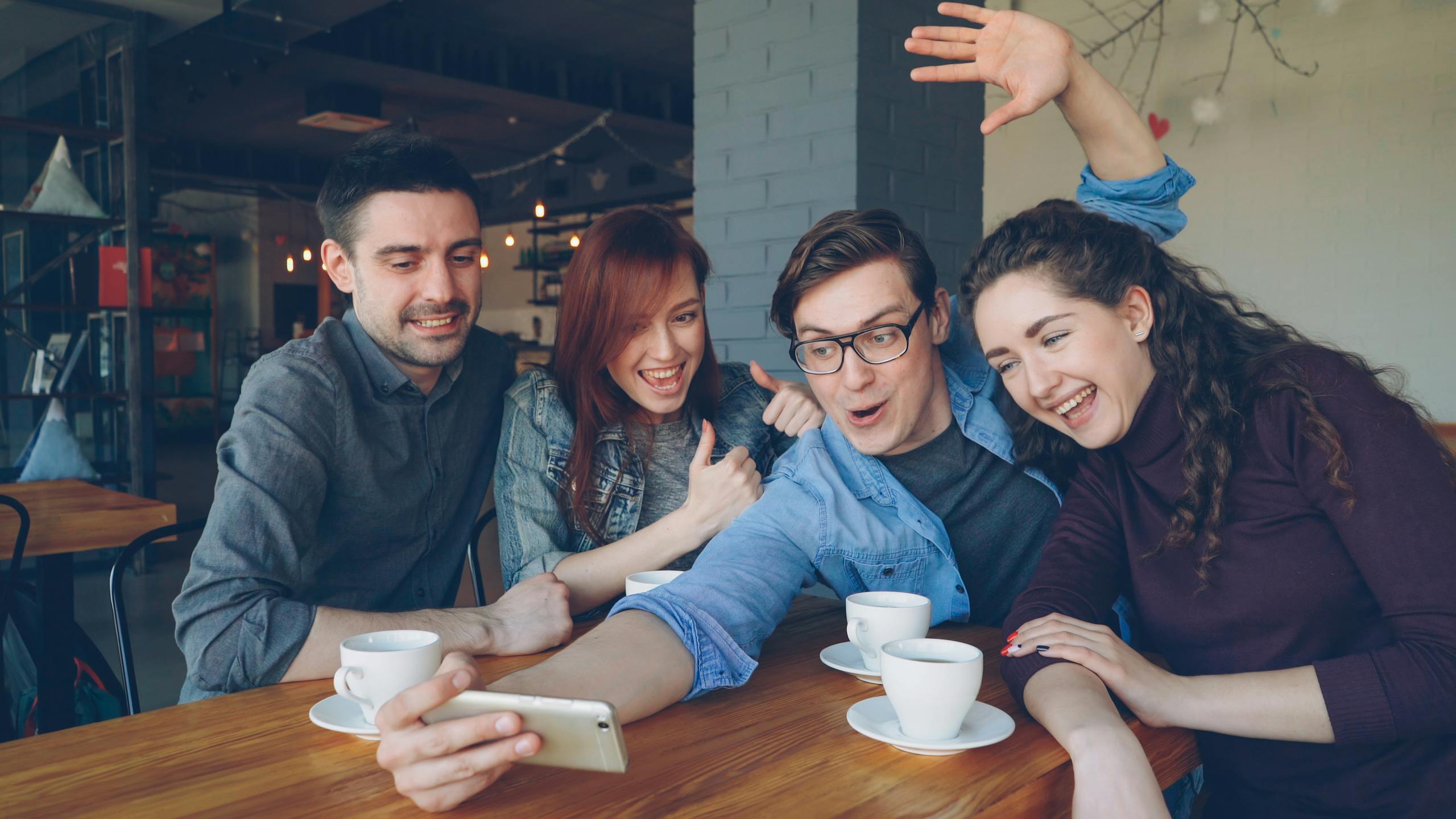 Group of friends having fun, drinking coffee, and taking a selfie in a café.