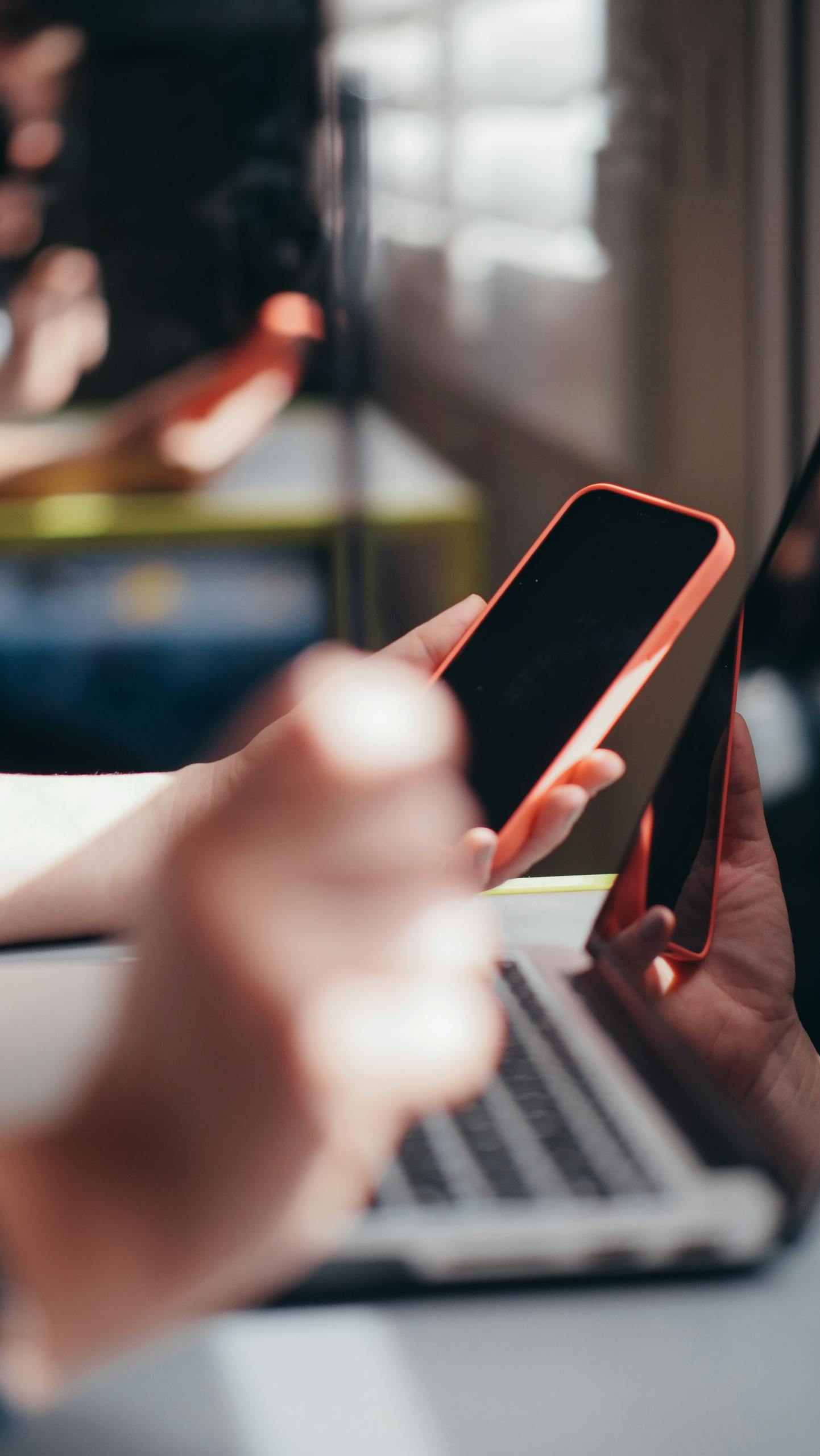 Hands holding smartphone near laptop, showcasing multitasking and technology use.