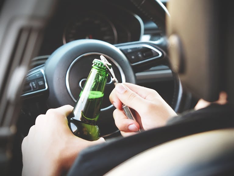 Hands opening a beer bottle inside a car, highlighting the importance of safe driving and awareness of road dangers.