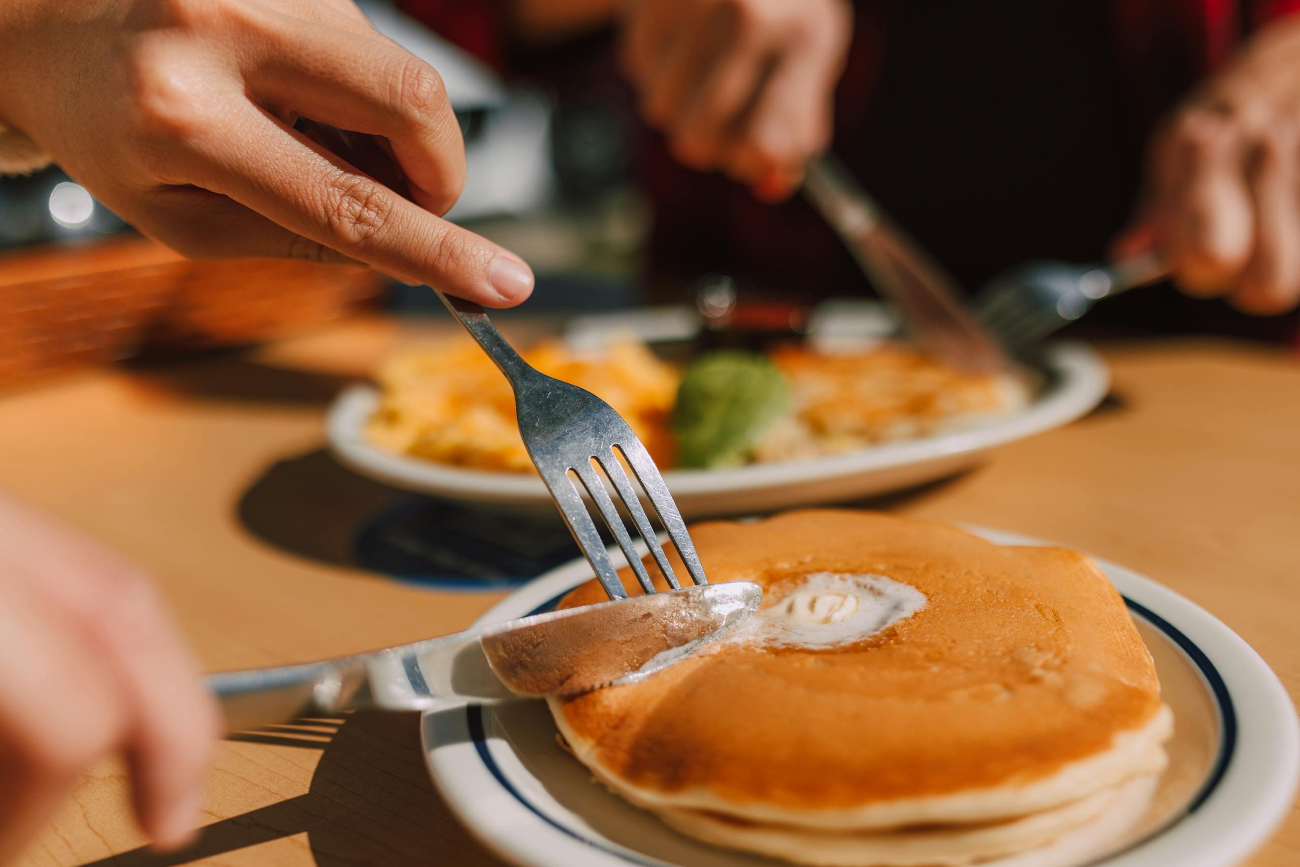 Hands slicing pancakes with butter, showcasing a delicious breakfast scene.