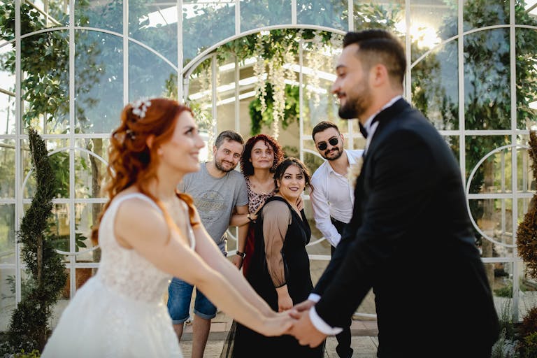 Happy bride and groom holding hands at a lively wedding in a beautiful greenhouse setting.