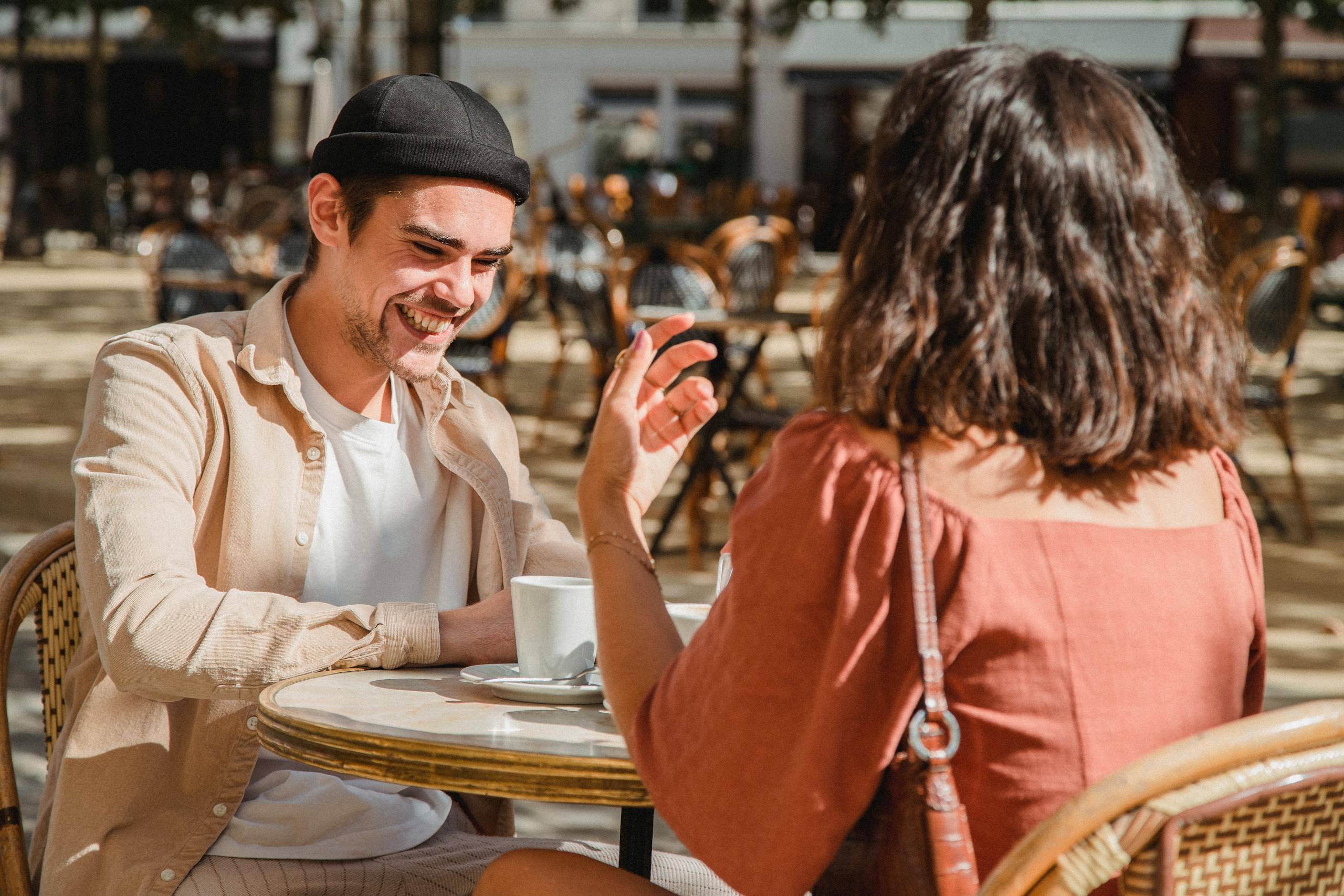 Happy couple enjoying a sunny day at an outdoor cafe, sharing laughter over coffee.