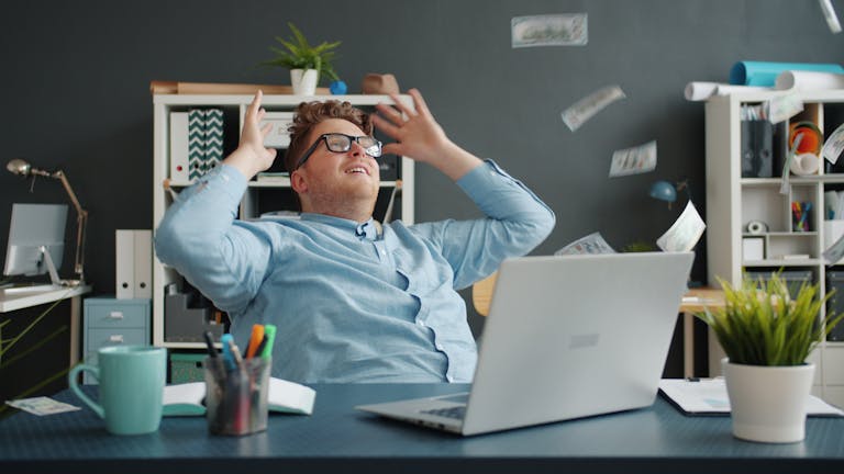 Happy office worker celebrates success at desk with money flying around.