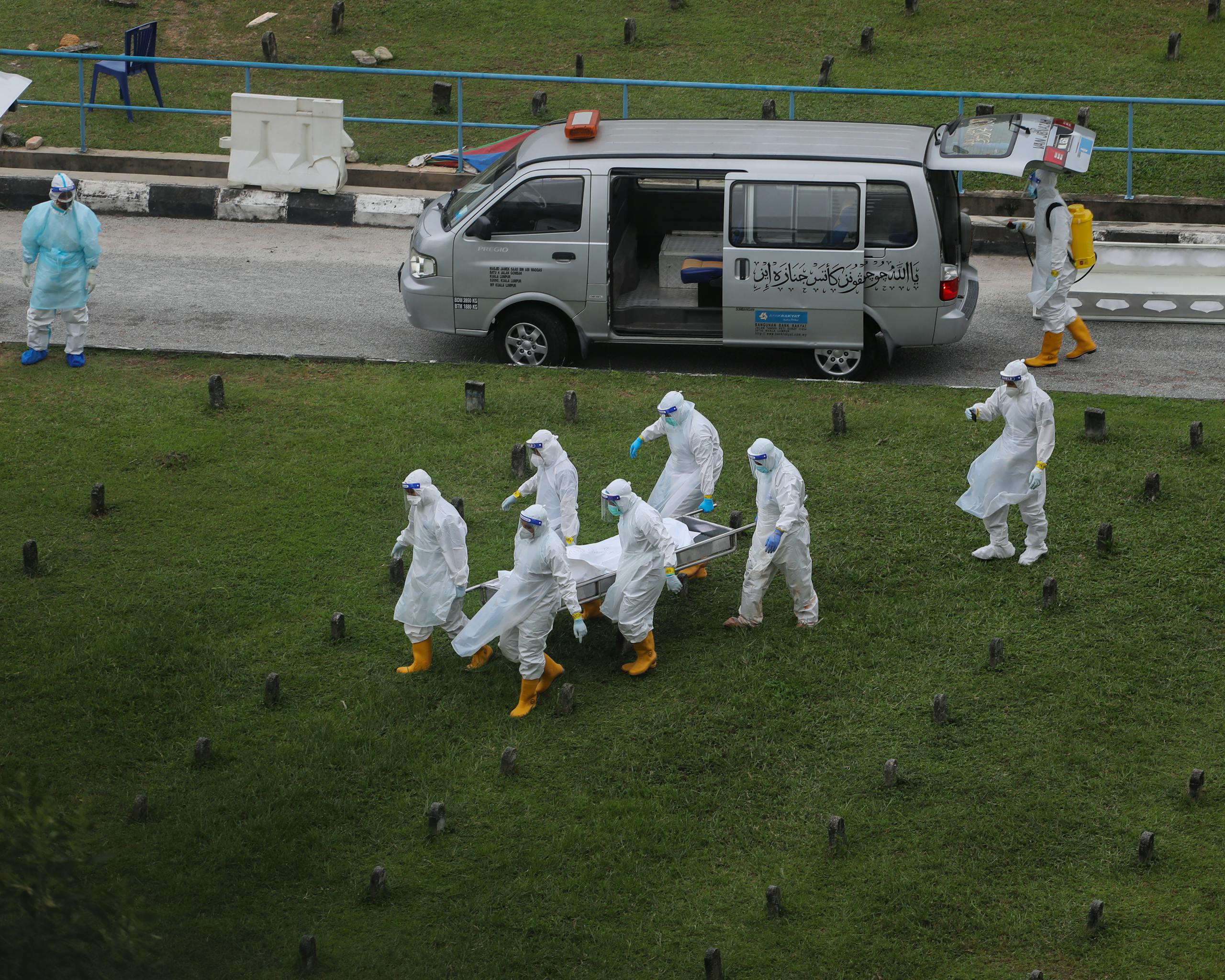 Healthcare workers wearing PPE carry a stretcher near a medical van in Kuala Lumpur.
