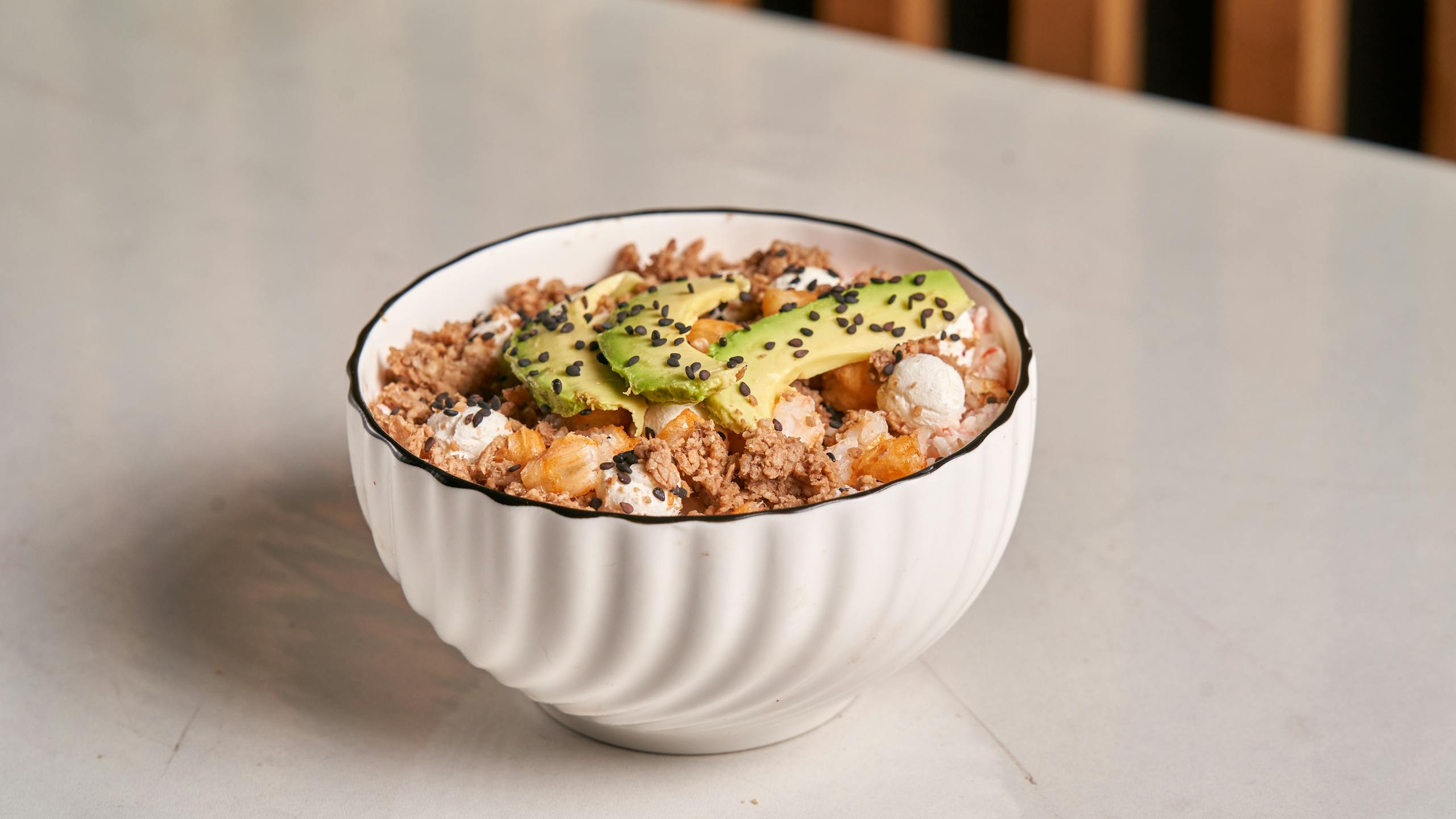 Healthy breakfast bowl featuring avocado, granola, and sesame seeds in a white dish.