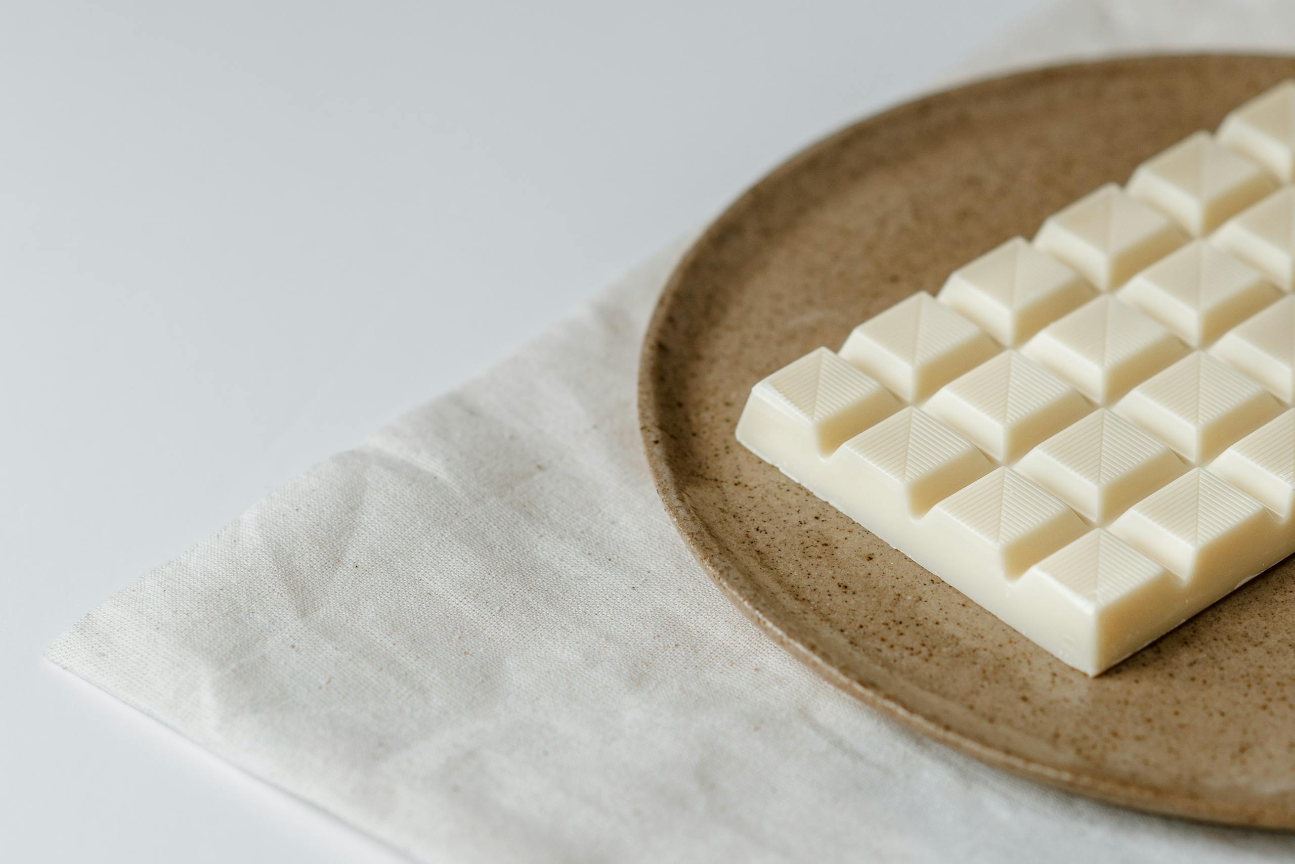 High angle of modern ceramic plate with bar of white chocolate on table