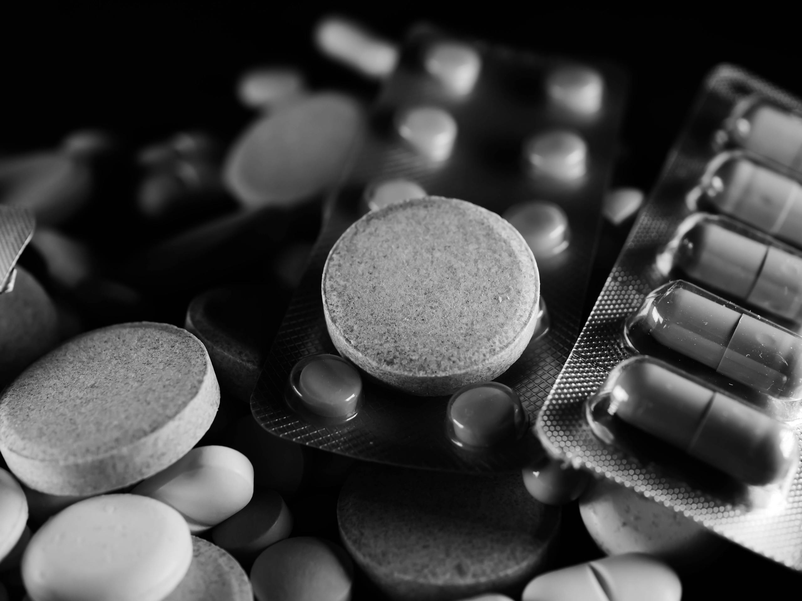 High-contrast close-up of assorted pills and capsules in black and white.