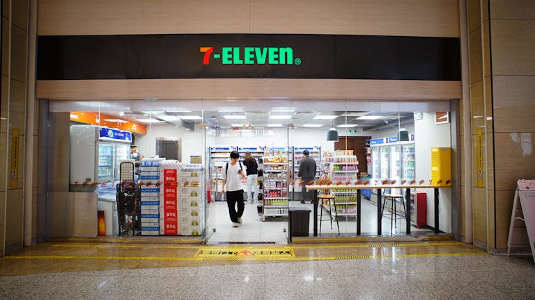 Indoor view of a 7-Eleven store entrance with people shopping and products displayed.