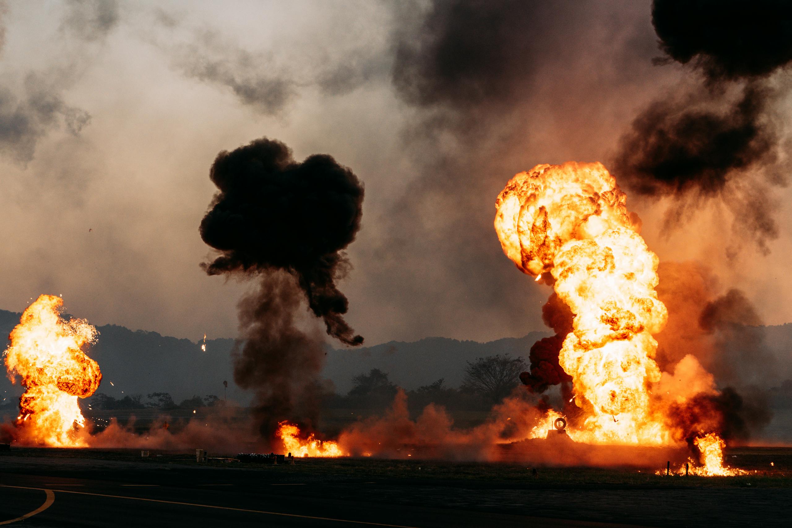 Intense fireball explosions with thick smoke in an outdoor setting. Captured during the day.