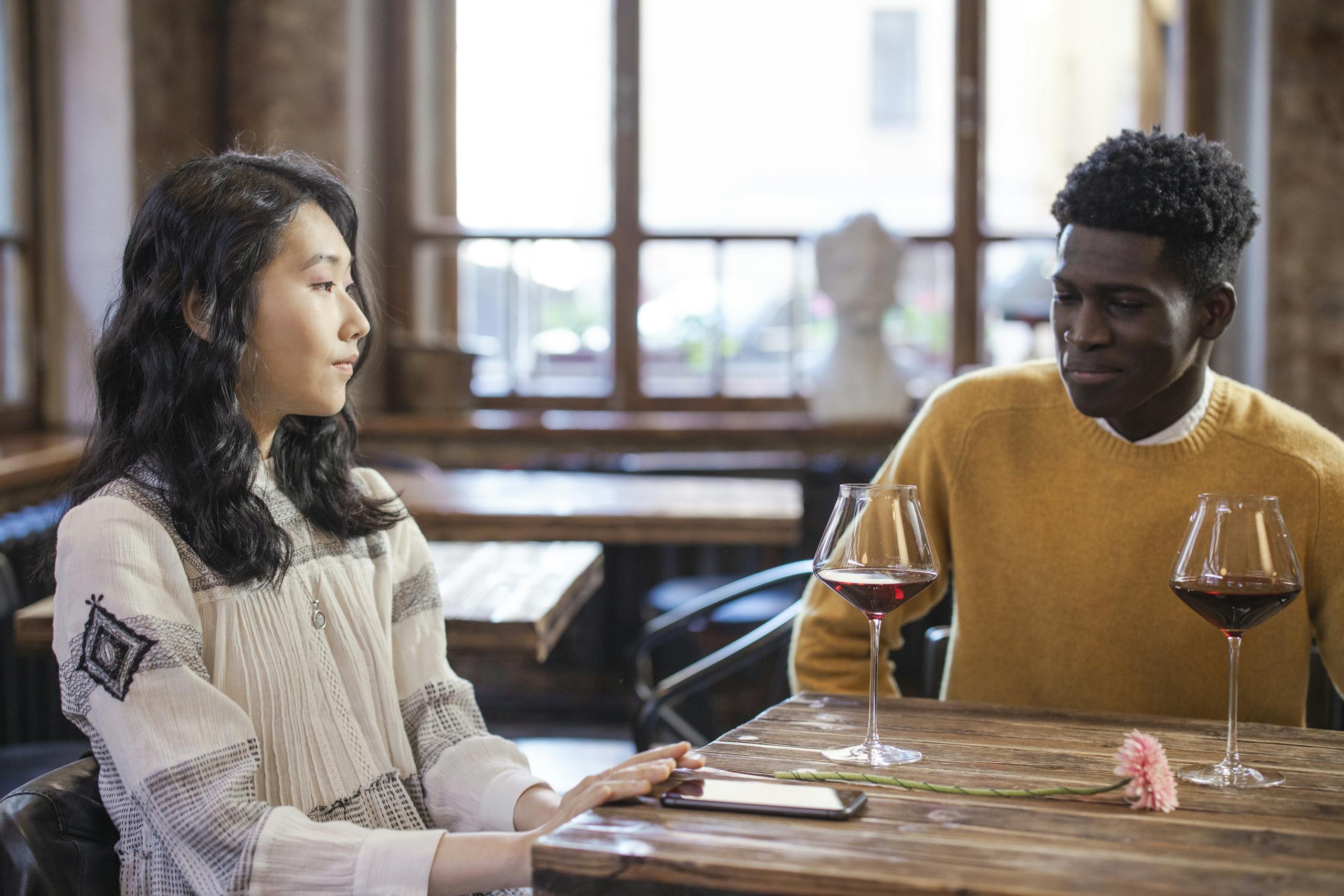 Interracial couple sharing a moment with red wine at a cozy restaurant table, indoors.