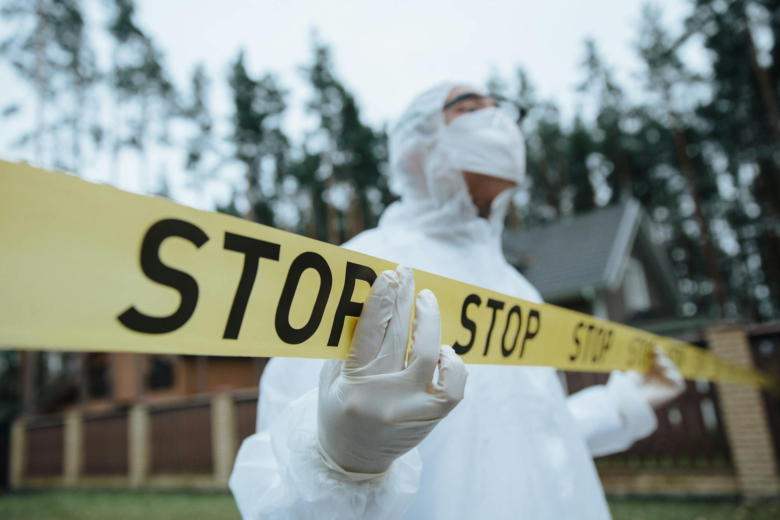 Investigator in protective gear securing crime scene with stop tape outdoors.