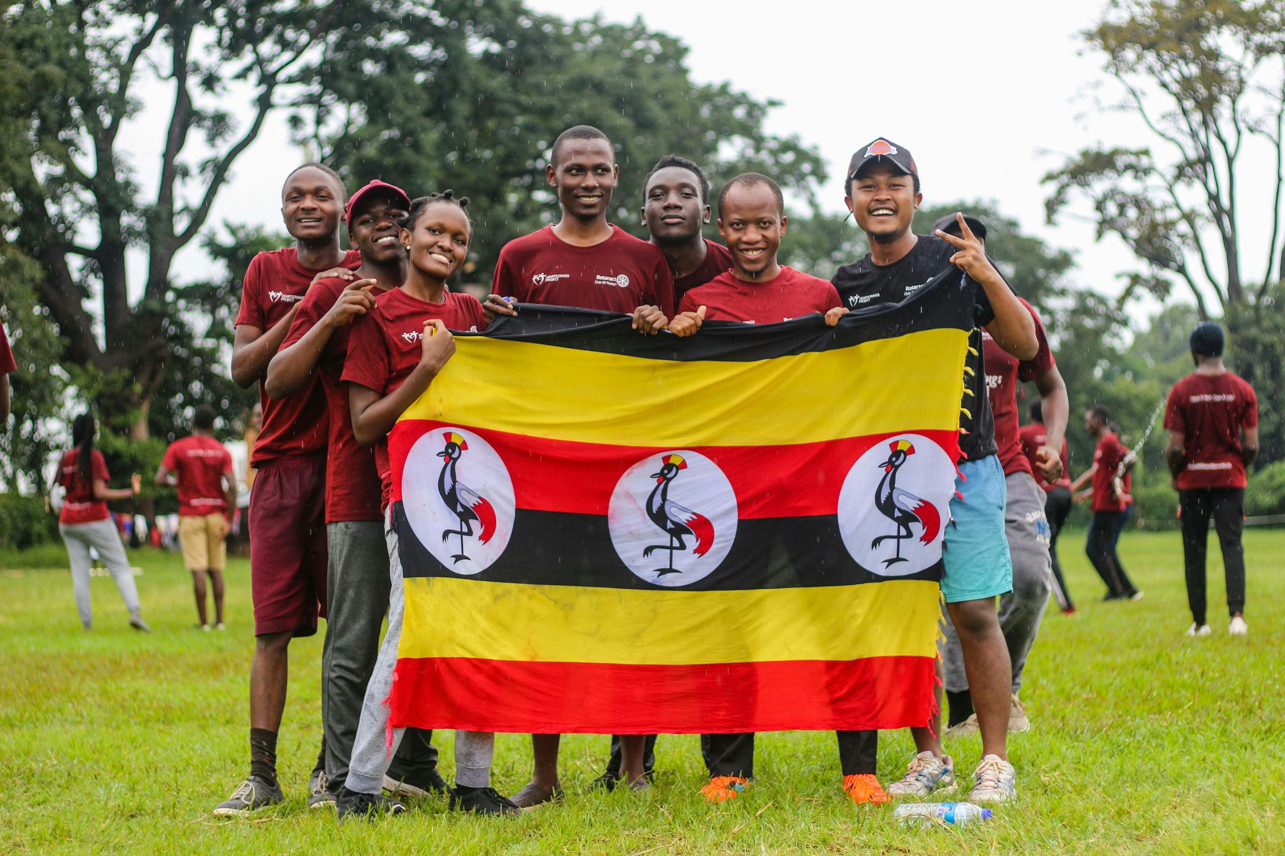 Joyful youth holding the Ugandan flag in a green outdoor setting, symbolizing unity and pride.