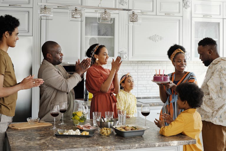 Joyous family birthday celebration with cake and clapping in a bright kitchen setting.