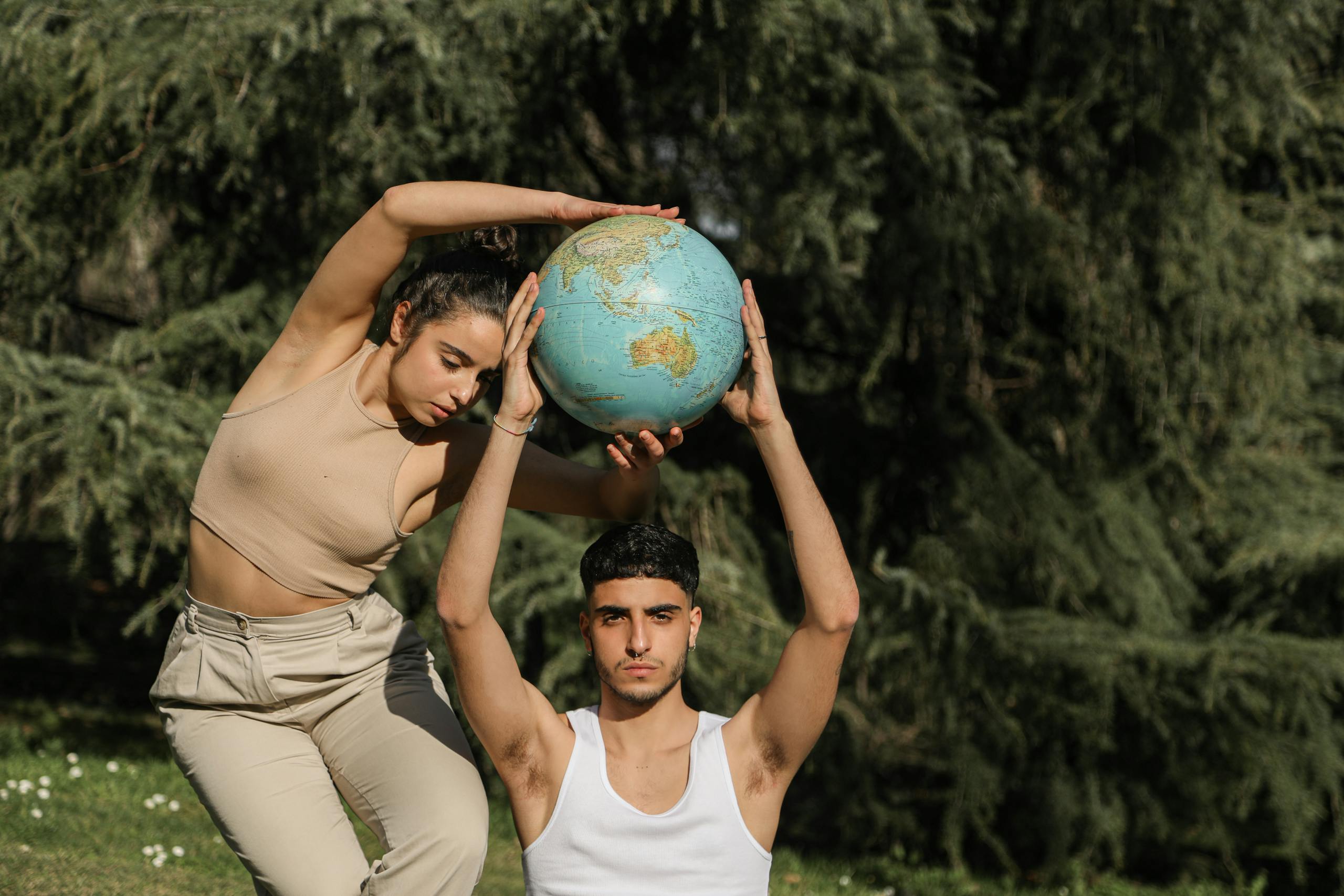 Man and woman artistically pose with a globe in a natural outdoor setting.