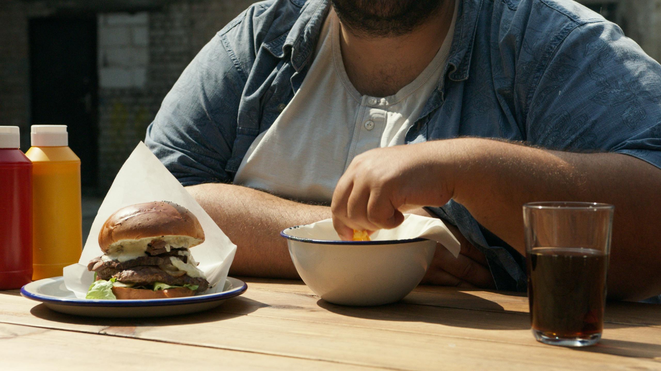 Man enjoys hamburger and fries at outdoor table in New York setting.