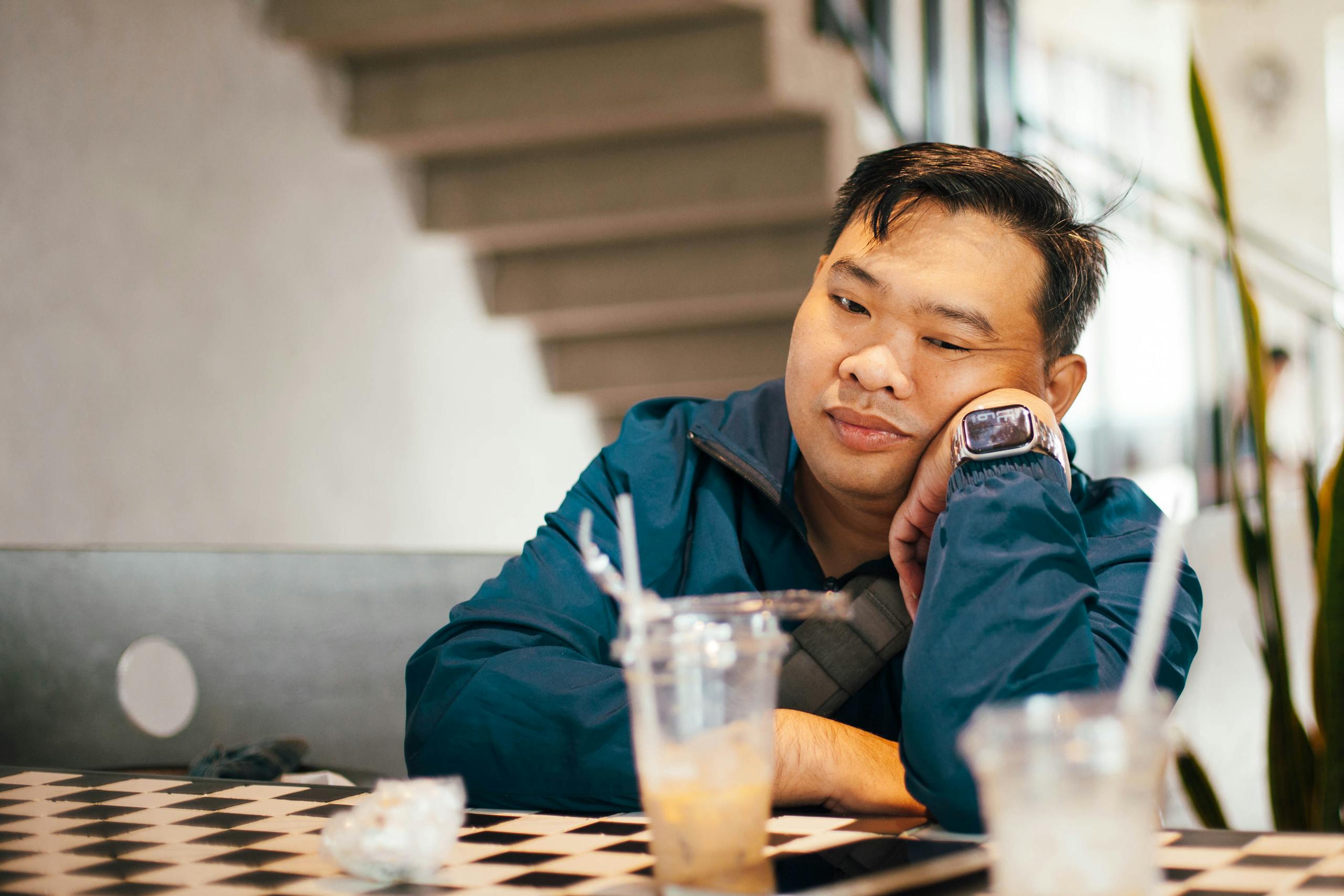 Man in casual wear sitting thoughtfully in a modern café, empty drink glasses on table.