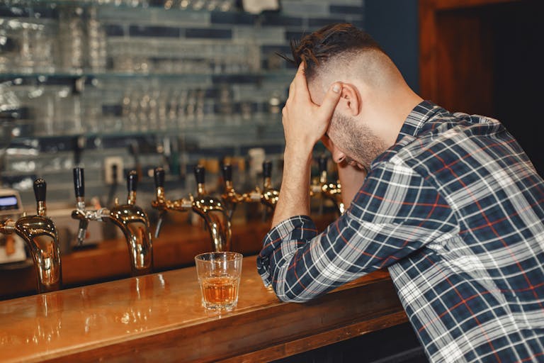 Man sitting at a bar counter with a glass of whiskey, appearing contemplative.