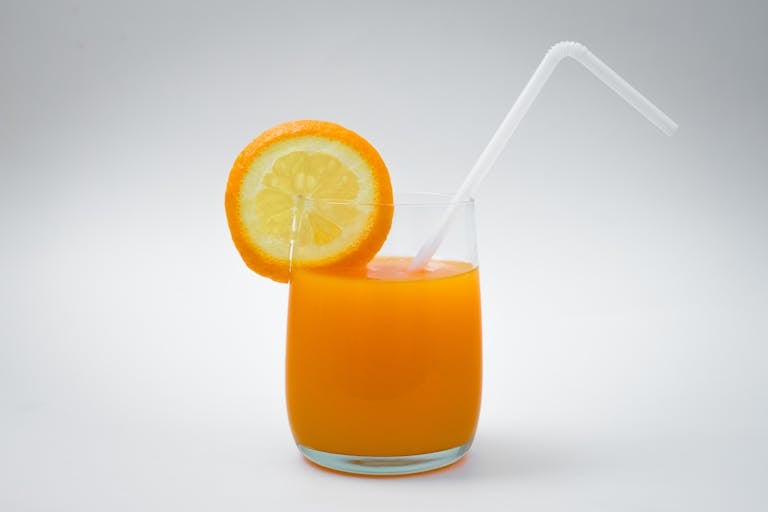Minimalist photo of a glass of orange juice with a refreshing slice and straw.