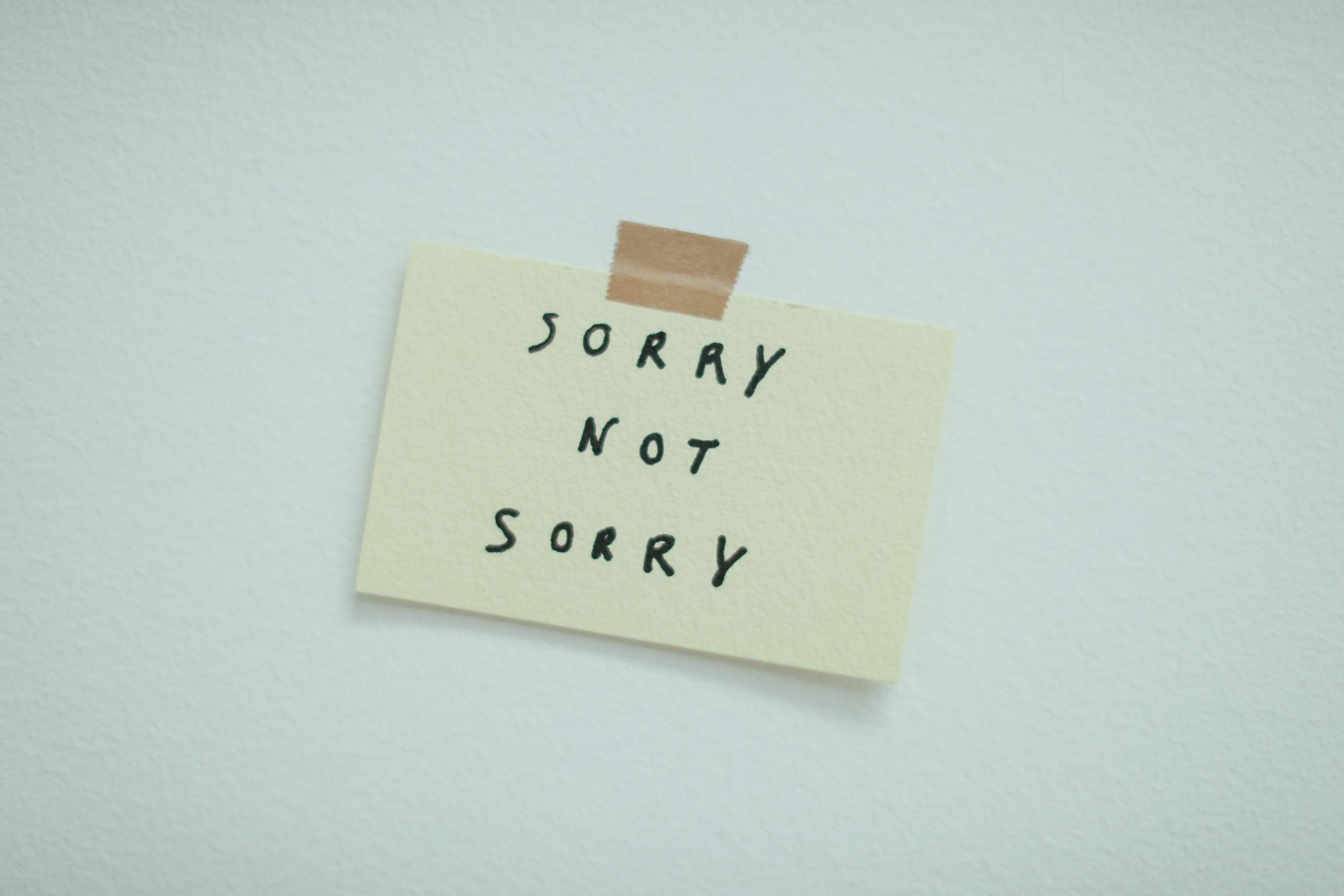 Minimalist post-it note taped to wall with phrase 'Sorry Not Sorry'.