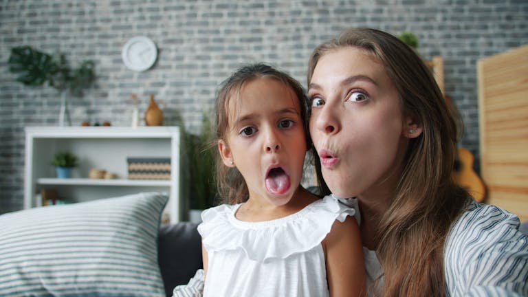 Mother and daughter having fun making silly faces in a cozy living room setting.