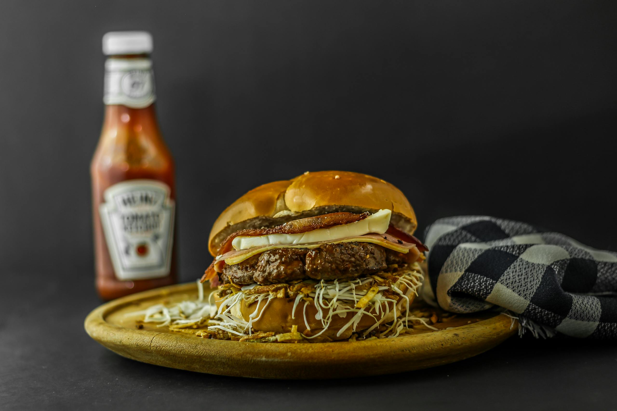 Mouth-watering gourmet burger with cheese and ketchup on wooden plate.