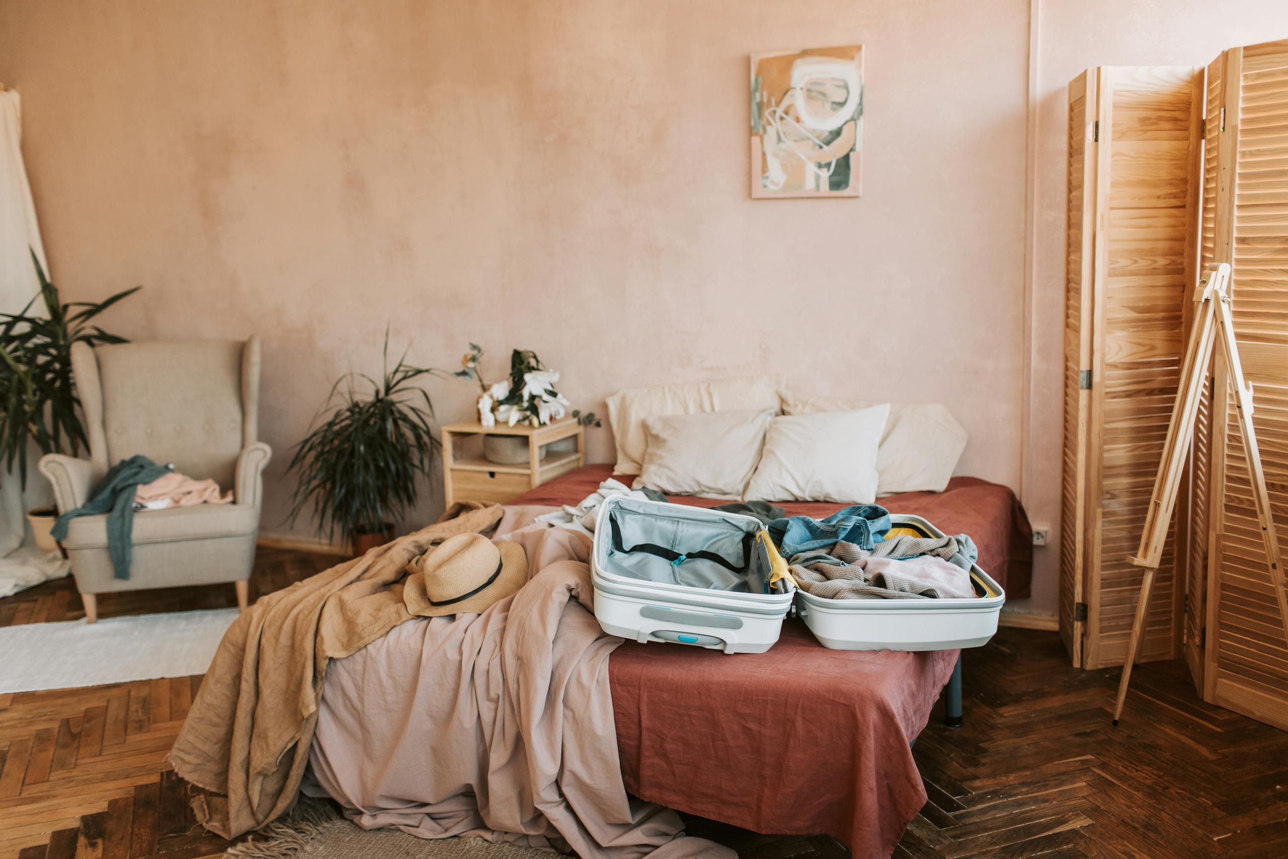Open suitcase on a bed in a cozy, warmly decorated bedroom, ready for travel.