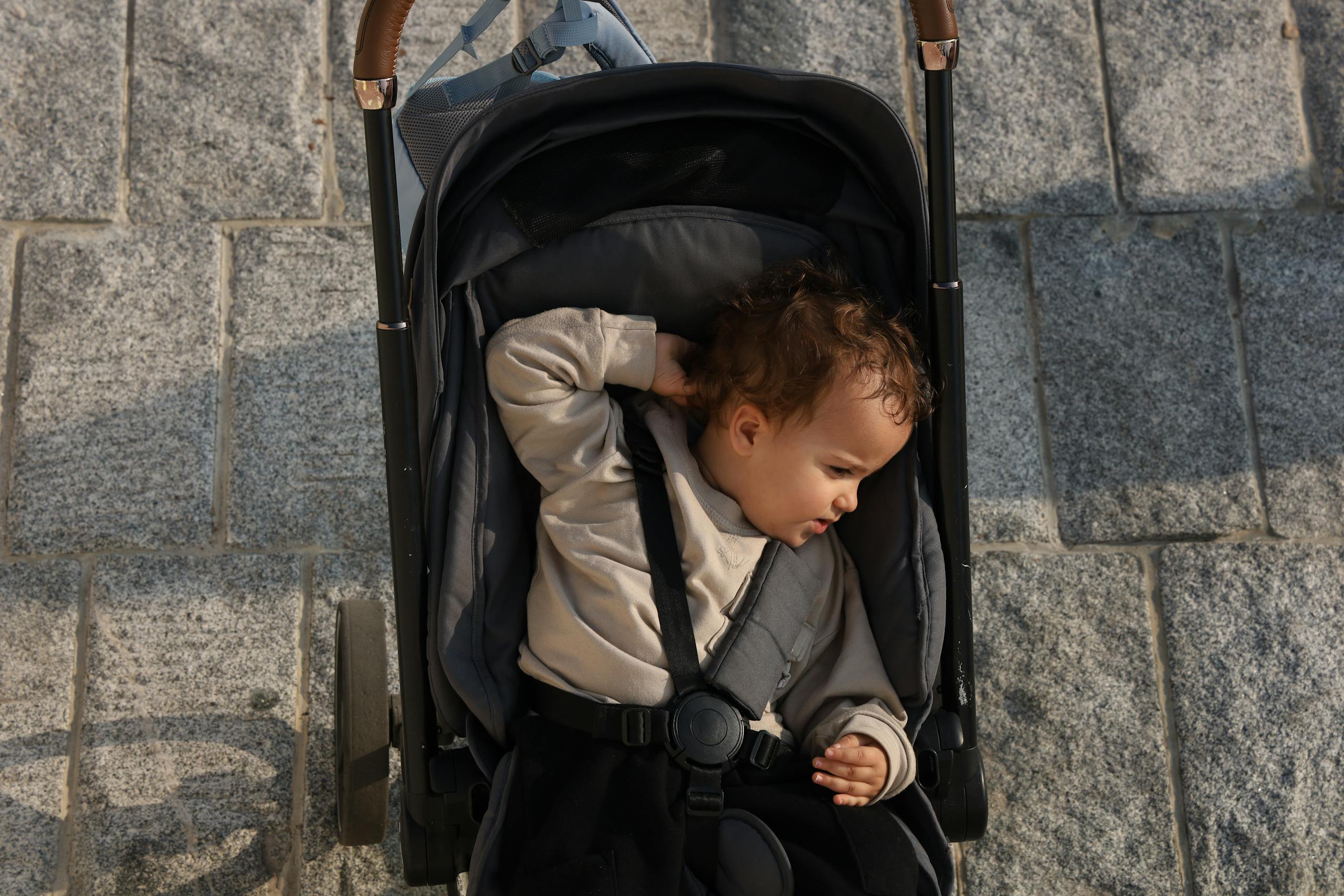 Overhead view of a baby in a stroller on a stone pavement, enjoying a sunny day.