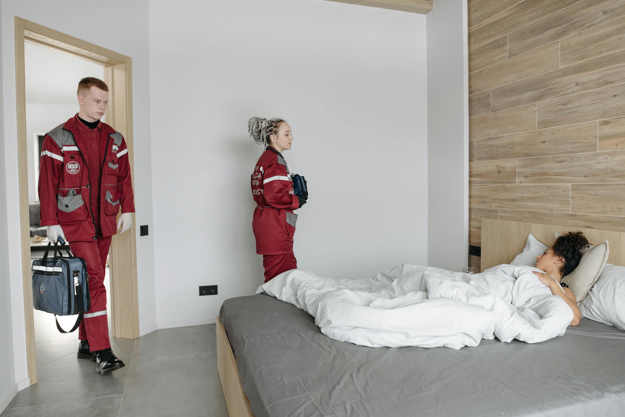 Paramedics assisting an unwell woman lying in bed, showcasing medical intervention indoors.
