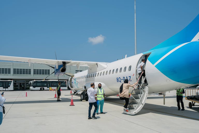 Passengers board a blue and white ATR 72 aircraft at an airport under clear skies.