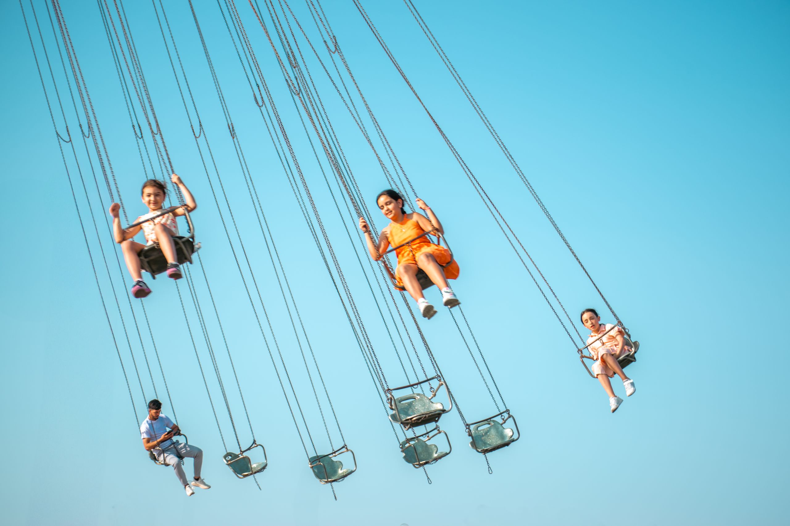 People enjoying a swing carousel ride against clear blue sky in summer.