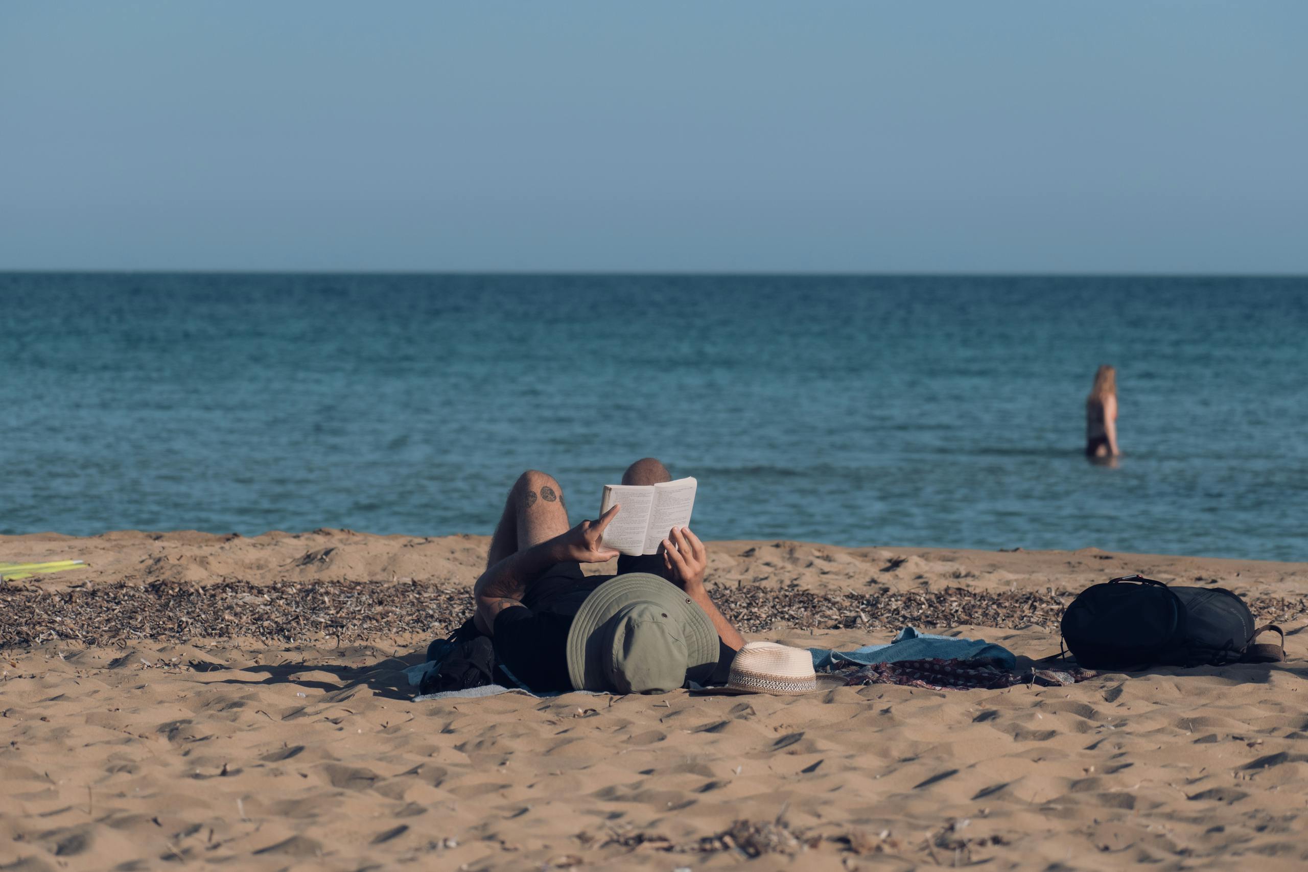 Person enjoying a peaceful day reading on a sandy beach with a clear ocean view.