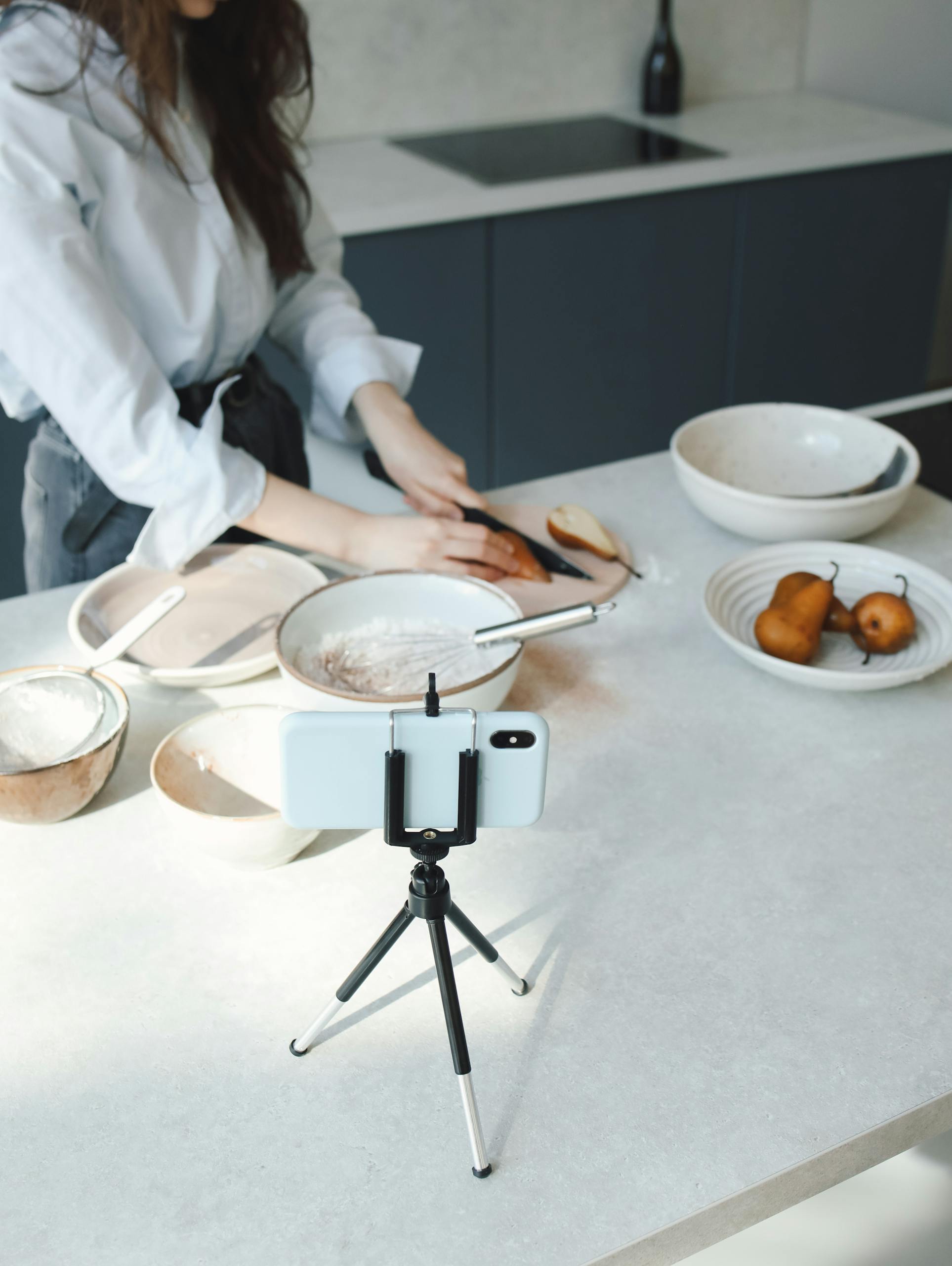 Person recording a cooking session with smartphone and tripod on a kitchen counter.