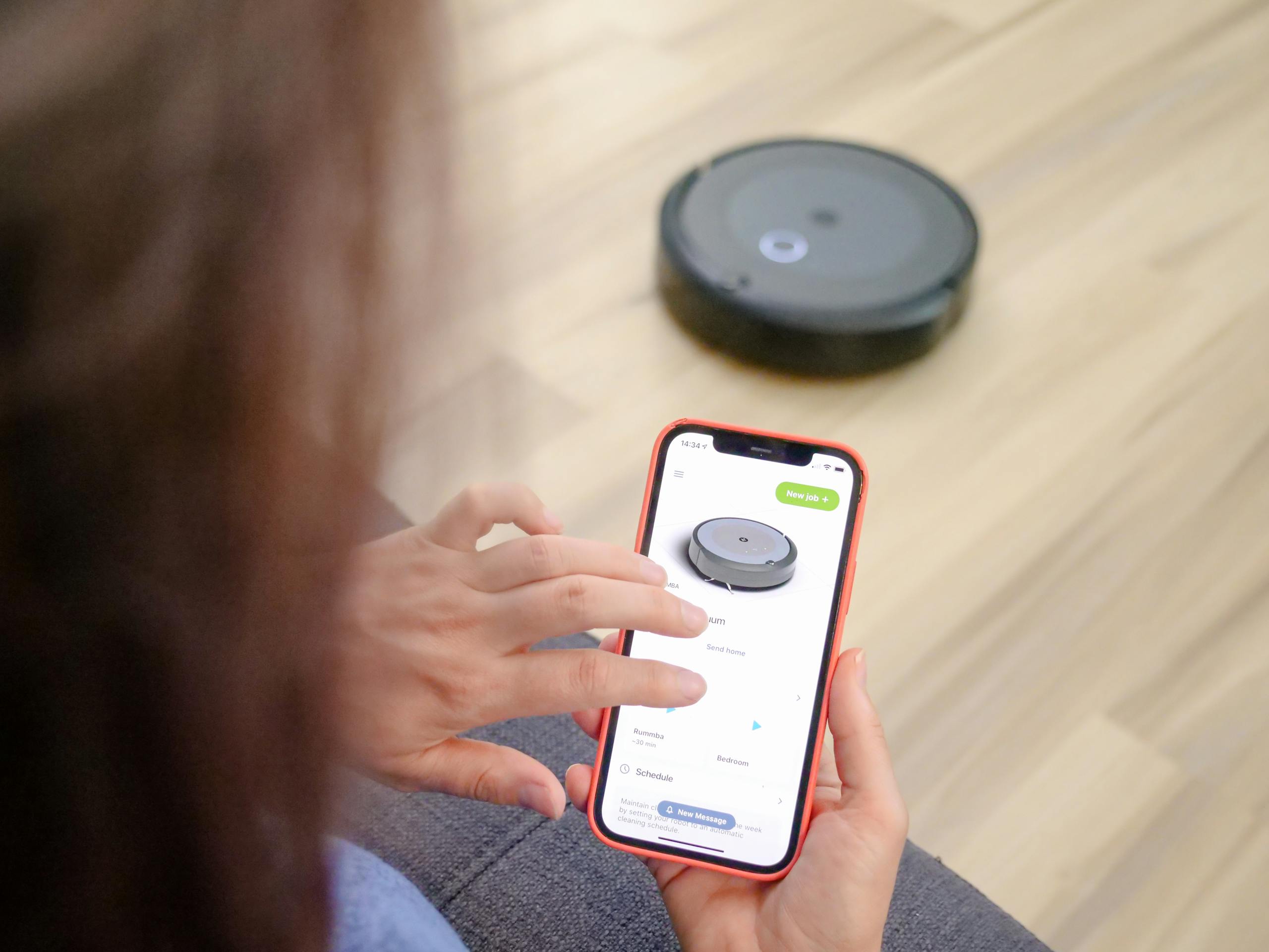 Person using smartphone app to remotely control a robotic vacuum cleaner.