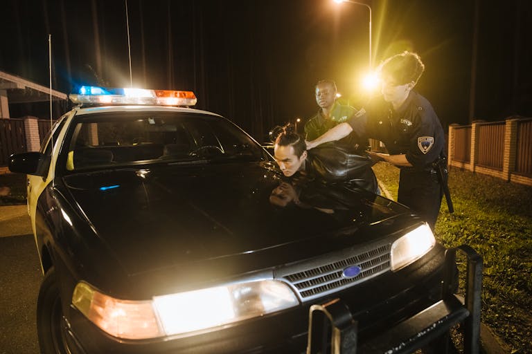 Police officers apprehending a suspect at night under streetlights by a patrol car.