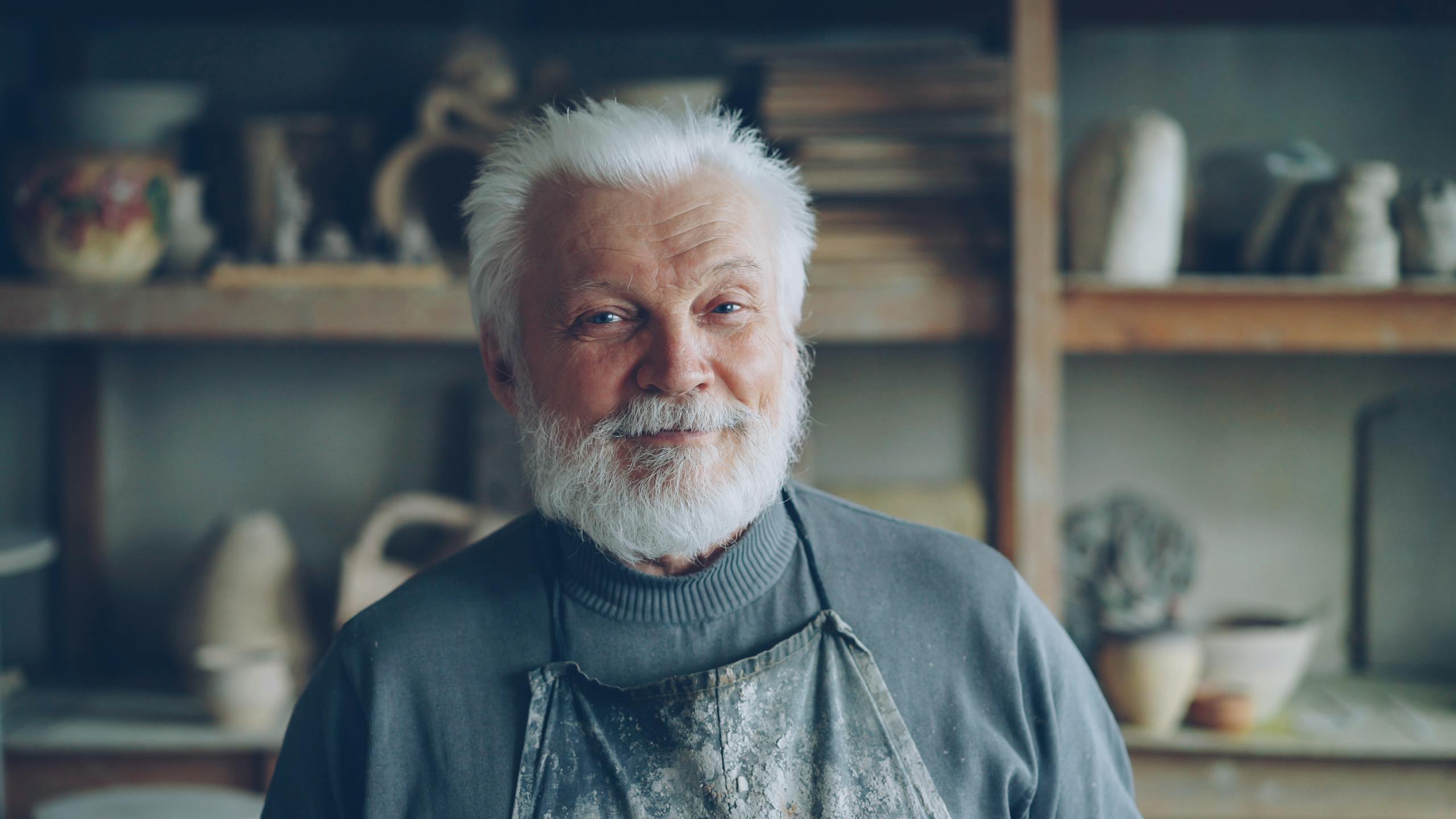Portrait of a senior male potter smiling in his workshop.
