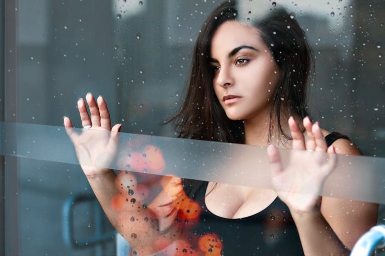 Portrait of a thoughtful woman standing behind a glass window on a rainy day in Santos, Brazil.