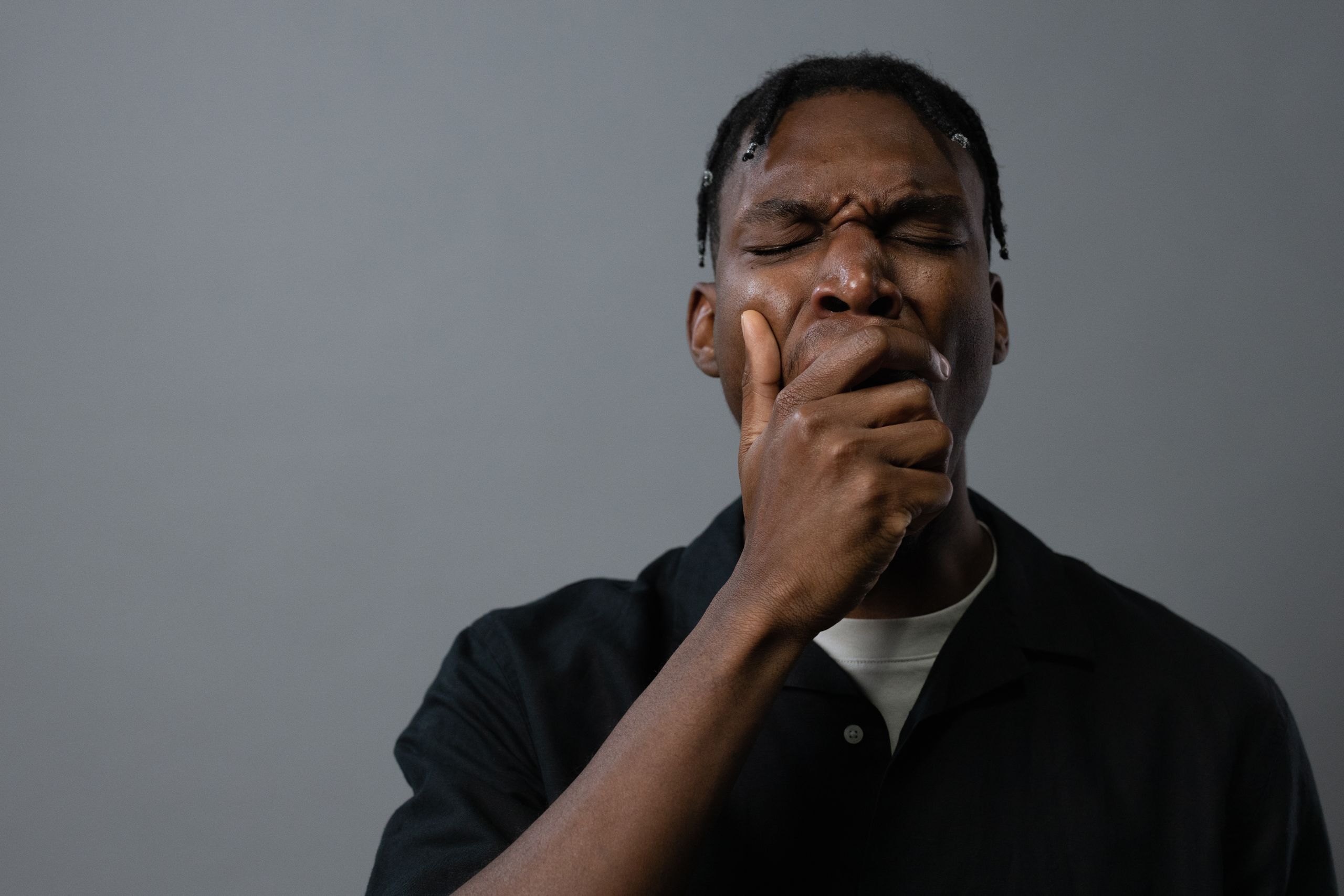Portrait of a tired man yawning with hand on mouth, showing fatigue and exhaustion.