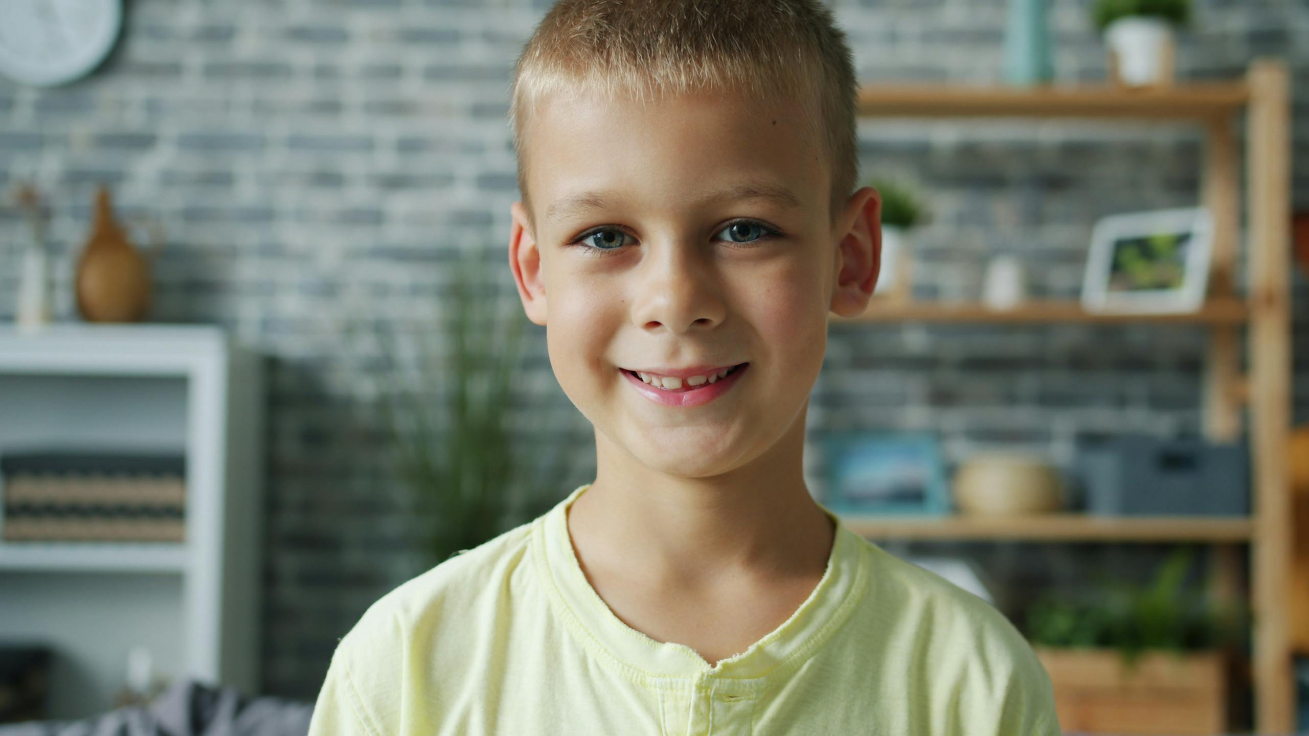 Portrait of a young boy smiling indoors against a brick wall background.