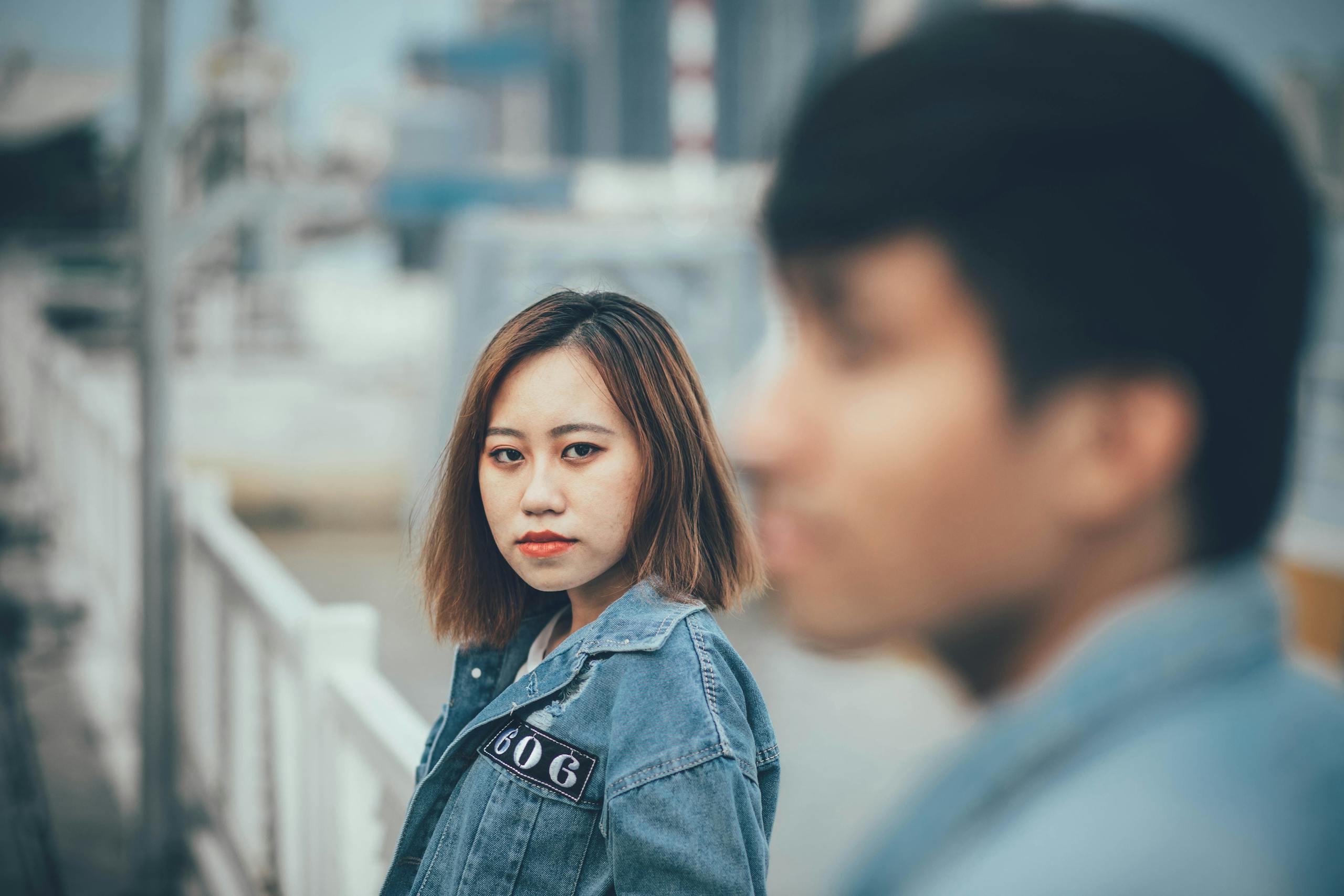 Portrait of a young woman in a denim jacket outdoors with urban background.