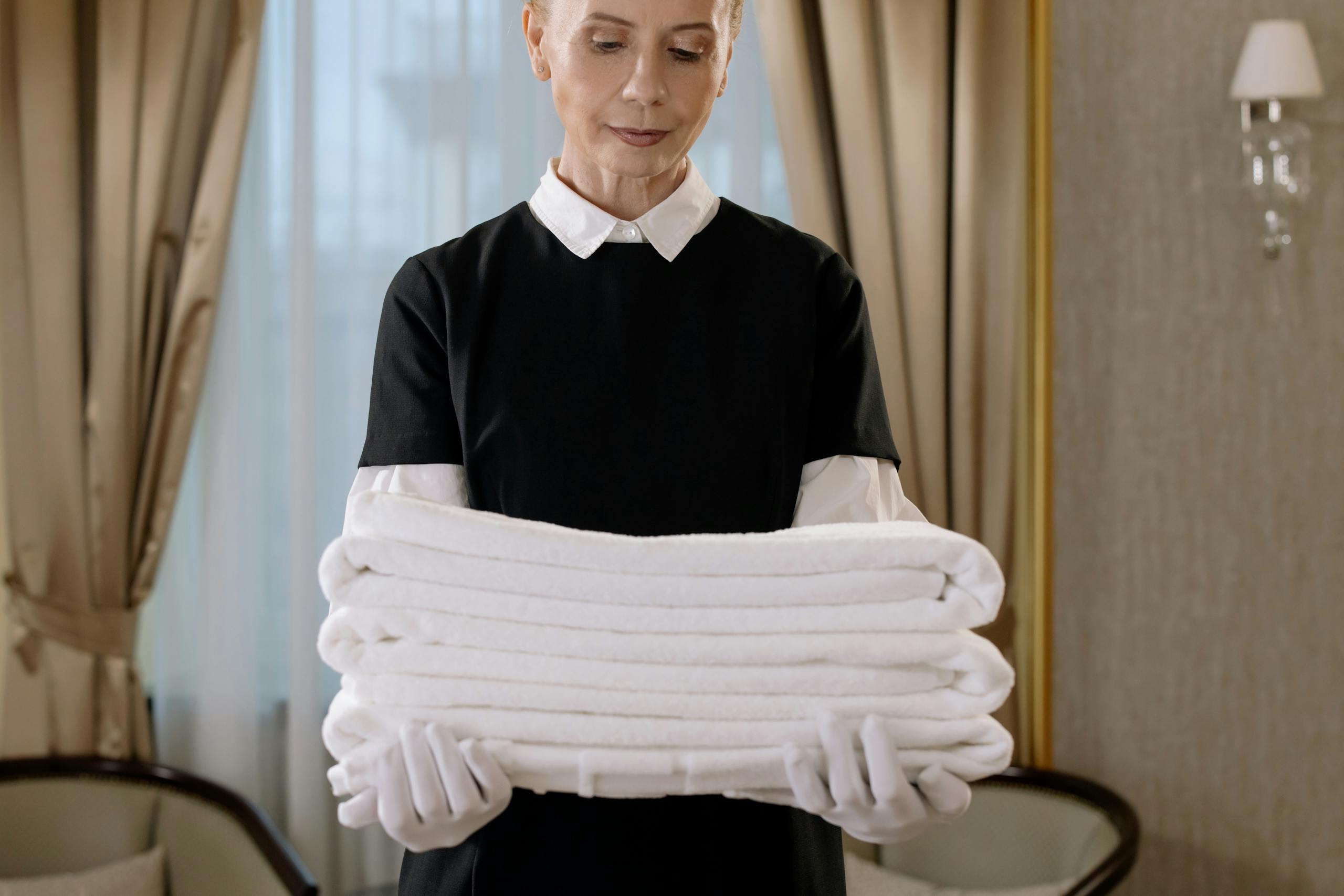 Professional housekeeper holding a stack of fresh towels in a luxurious hotel room, showcasing elegance and service.
