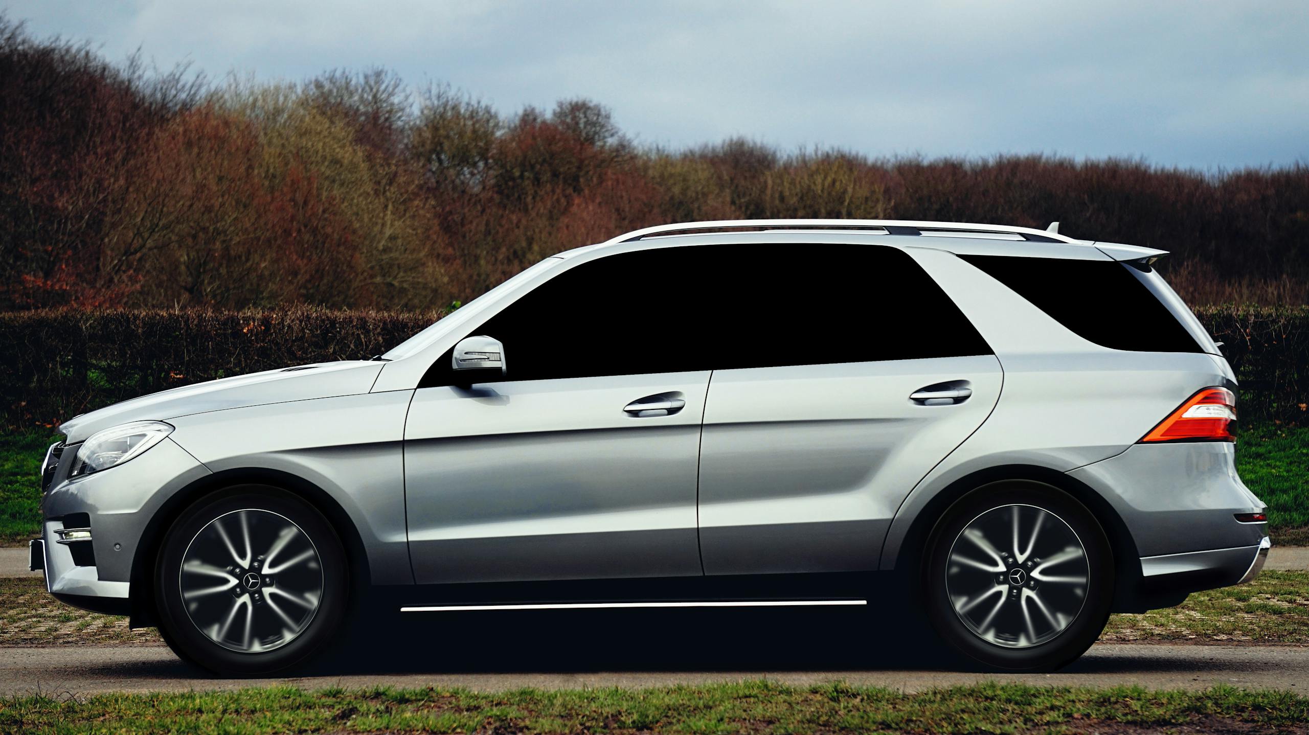 Profile of a sleek silver SUV parked on a rural road in autumn setting.