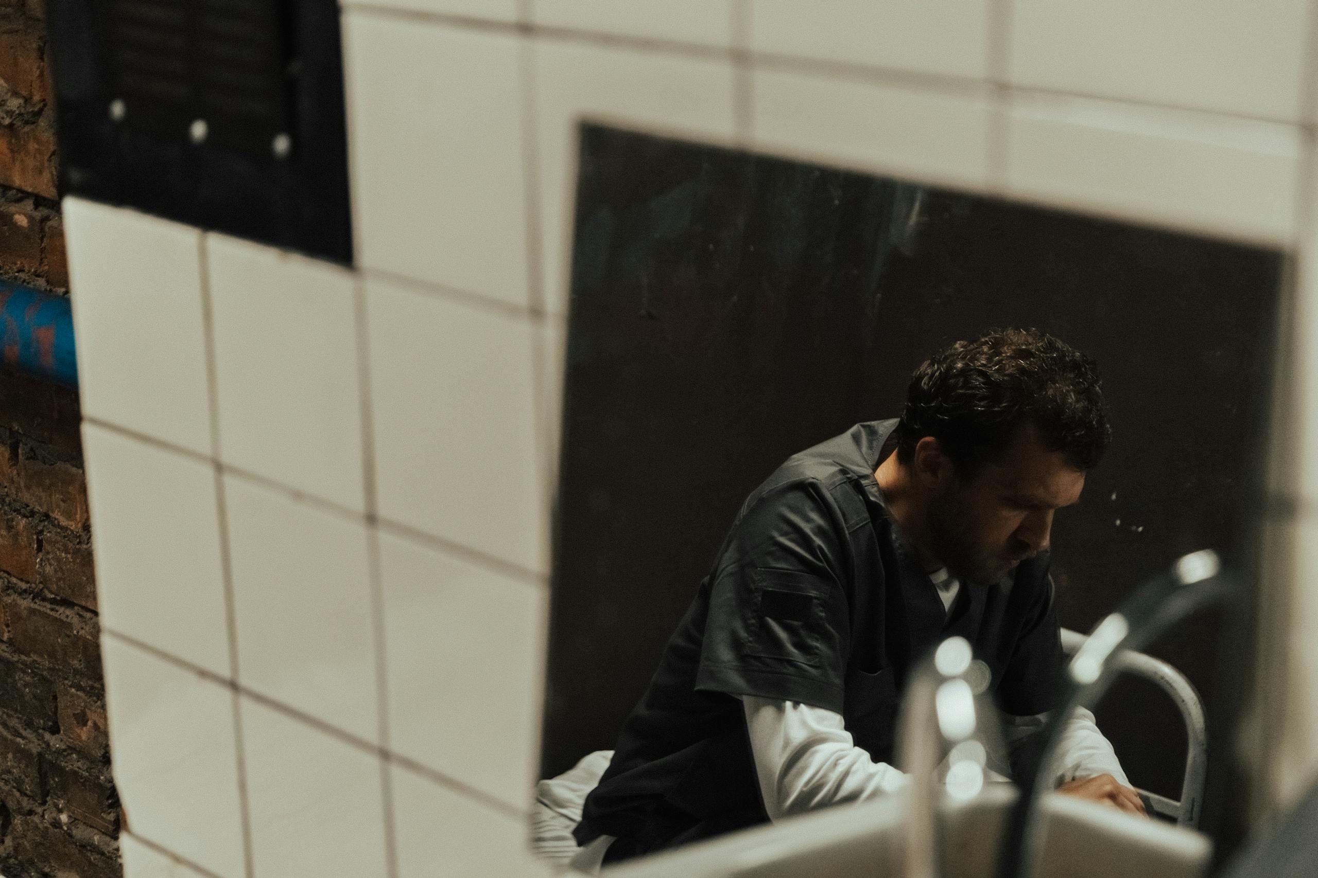 Profile of a solitary prisoner reflected in a mirror in a tiled jail cell.