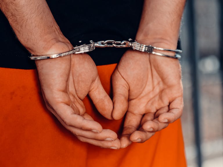 Rear view of handcuffed person in orange uniform, highlighting law enforcement and justice themes.