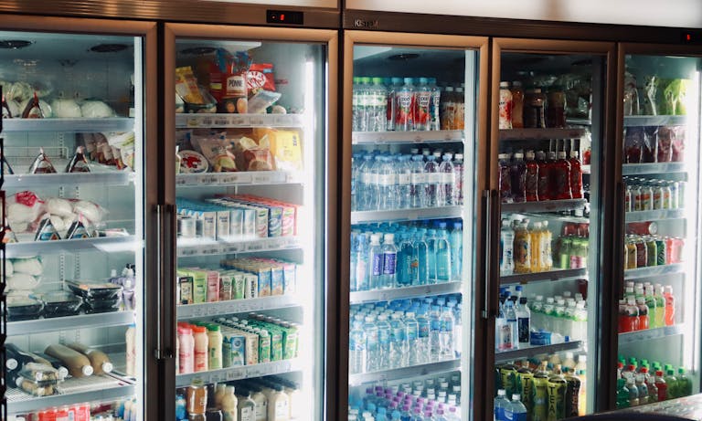 Refrigerator display with various beverages and snacks in a store environment.