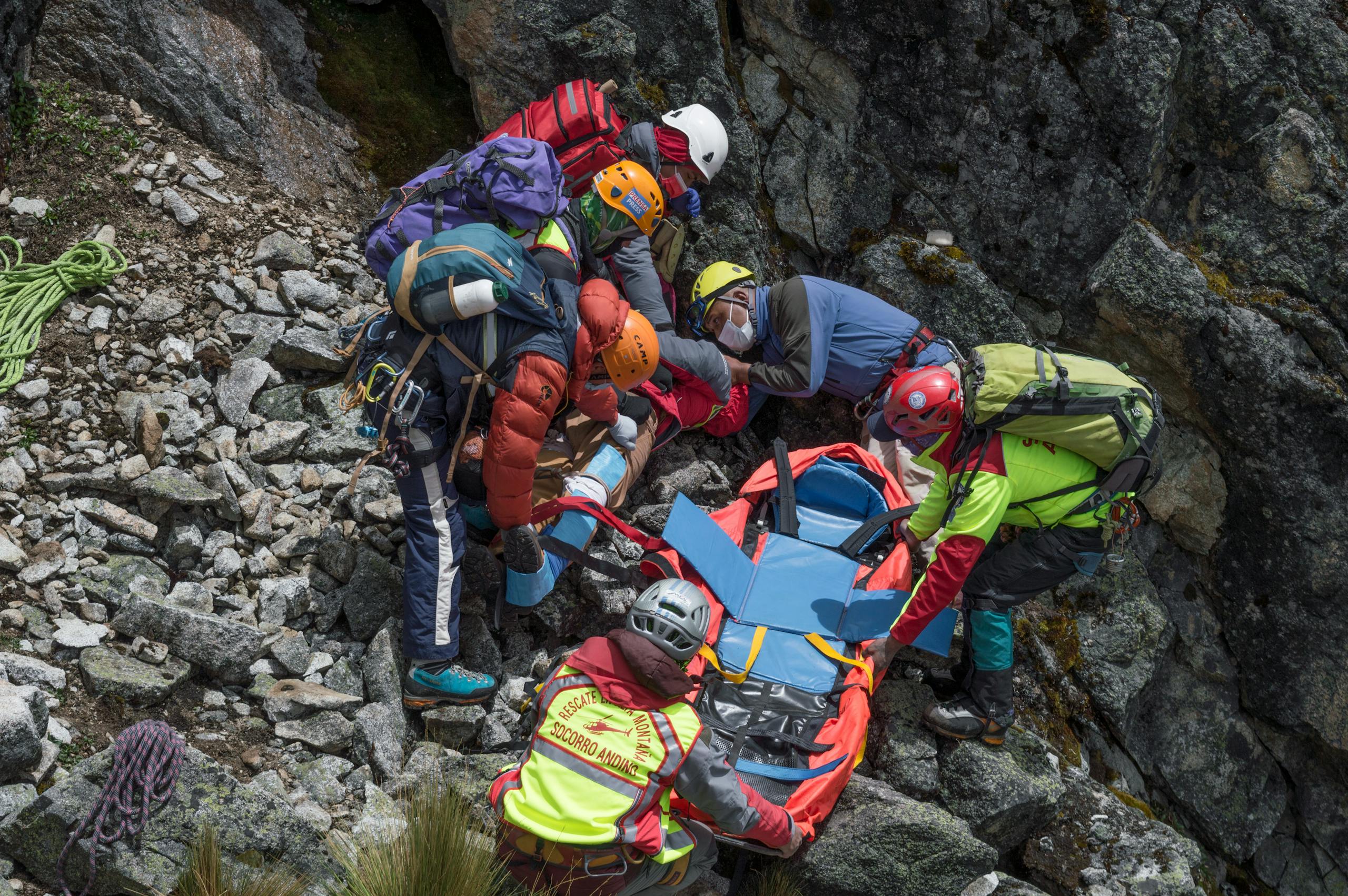 Rescue team assisting injured hiker on rocky mountainside with stretcher.