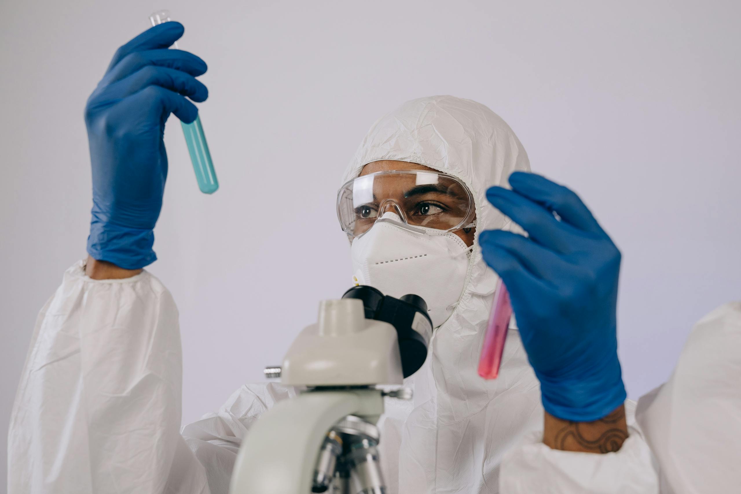 Research scientist wearing PPE observes test tubes in a secure laboratory setting.