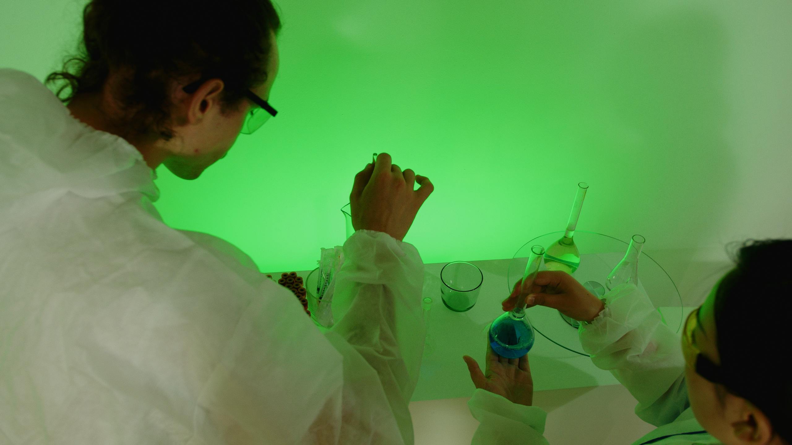 Researchers working together in a lab, mixing chemicals for an experiment under green lighting.