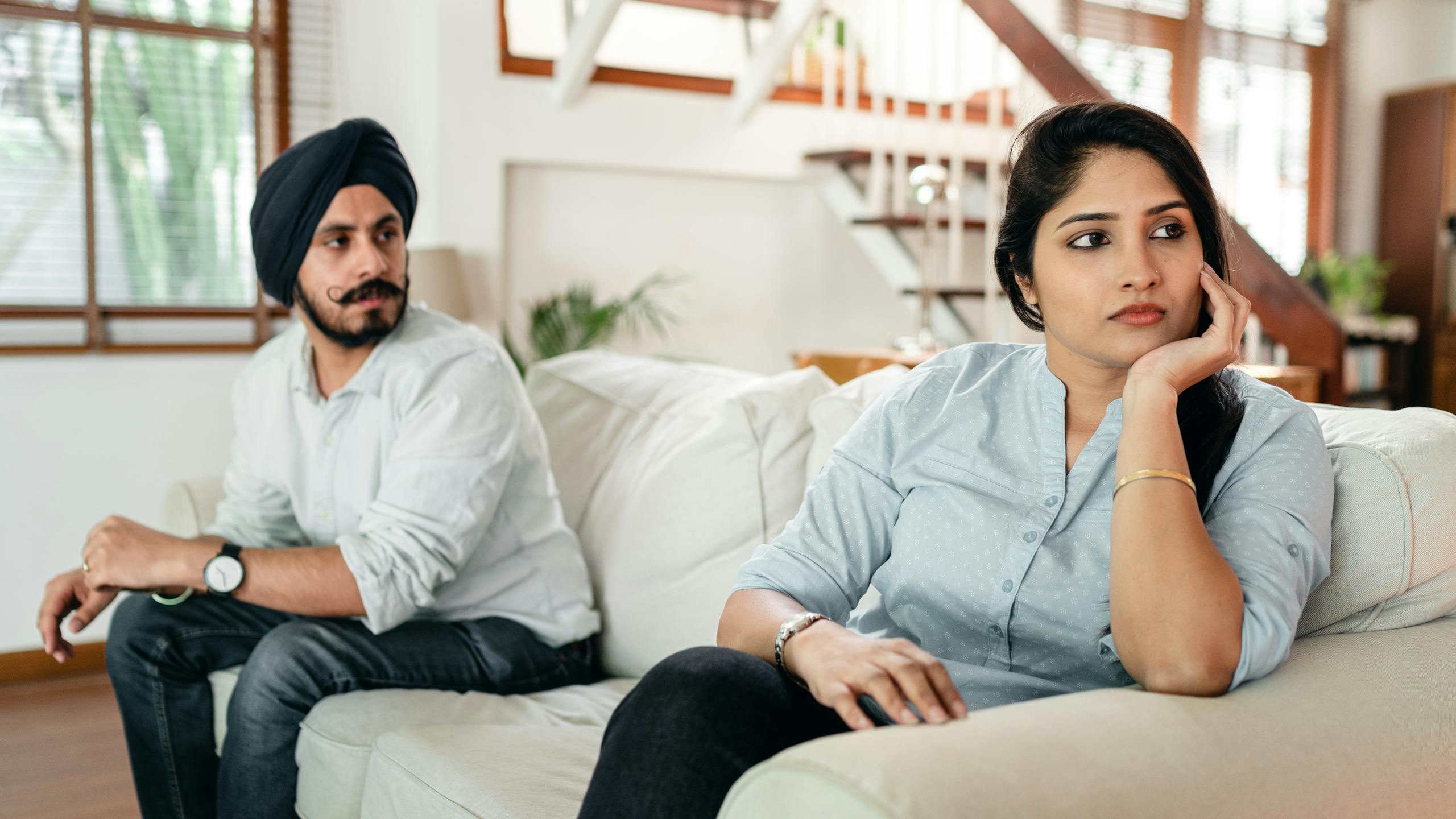 Resentful young Indian lady in casual wear ignoring husband in traditional turban during arguing at home